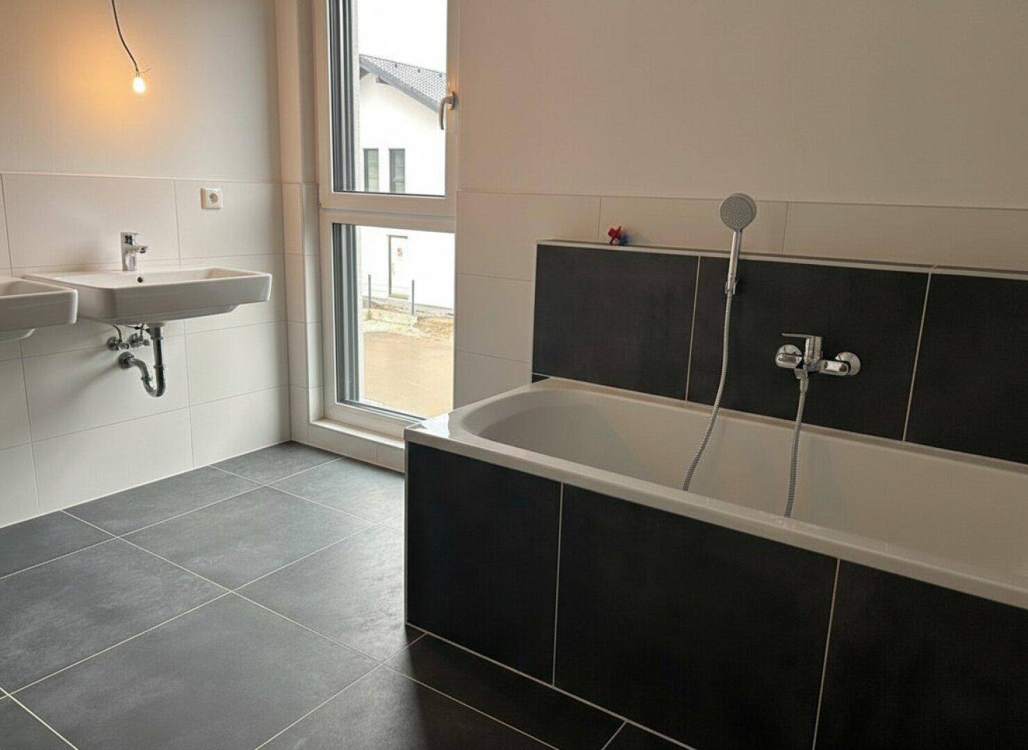 Modernes Badezimmer mit Badewanne, zwei Waschbecken und einem Fenster für Tageslicht.