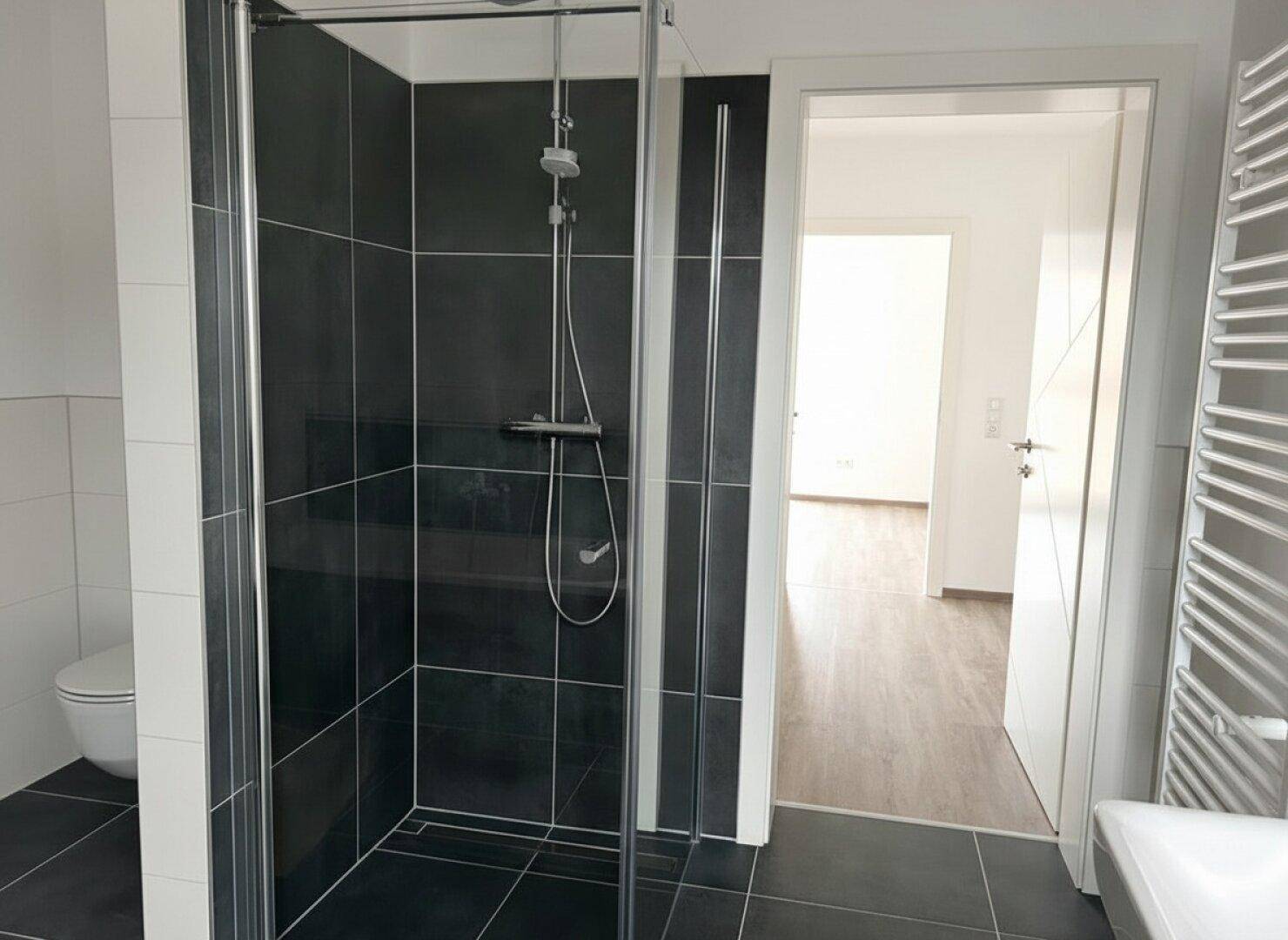 Modernes Badezimmer mit ebenerdiger Dusche, WC und beheiztem Handtuchhalter.