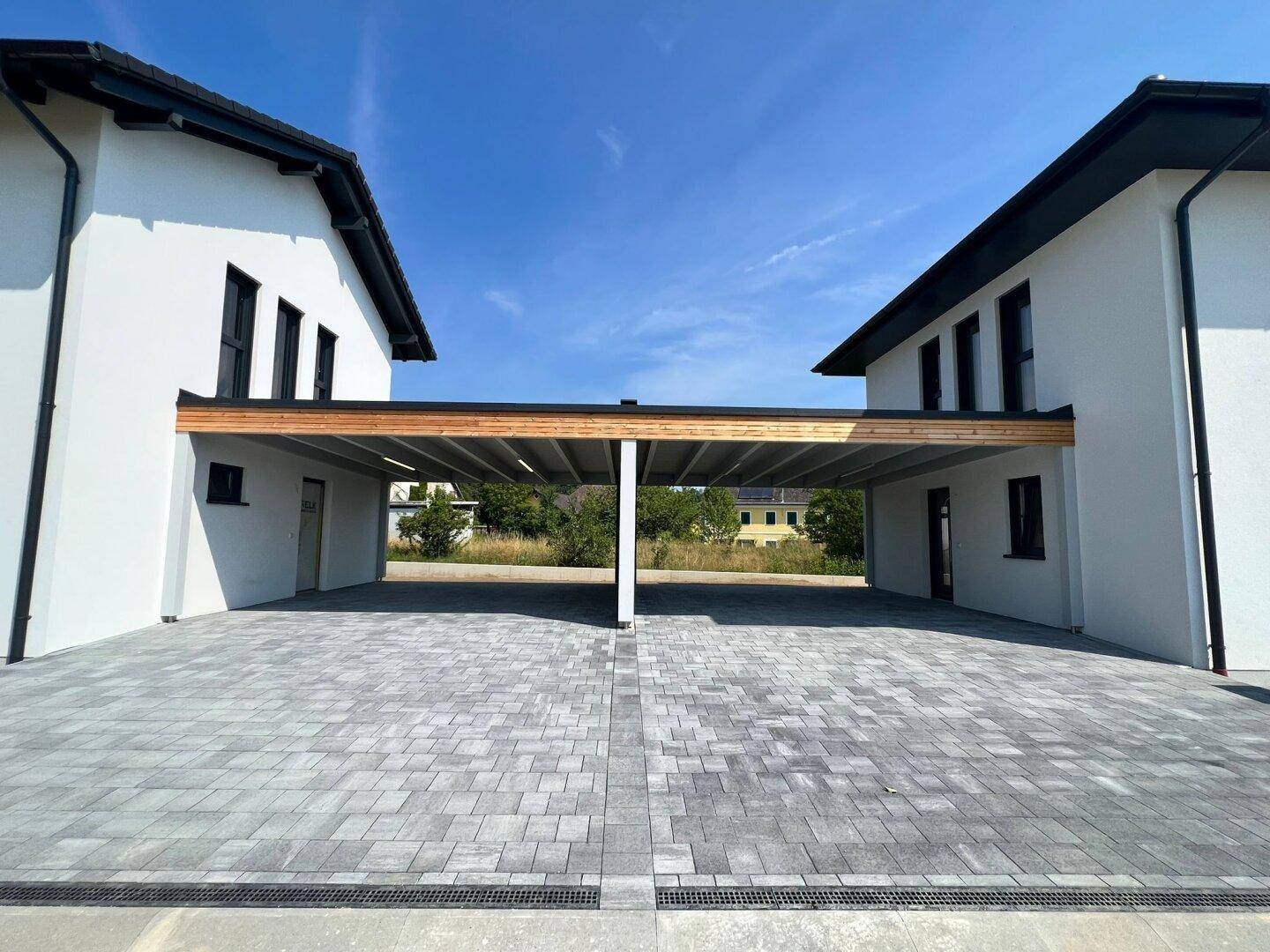 Zwei moderne Doppelhaushälften mit gemeinsamem Carport und gepflasterter Zufahrt.