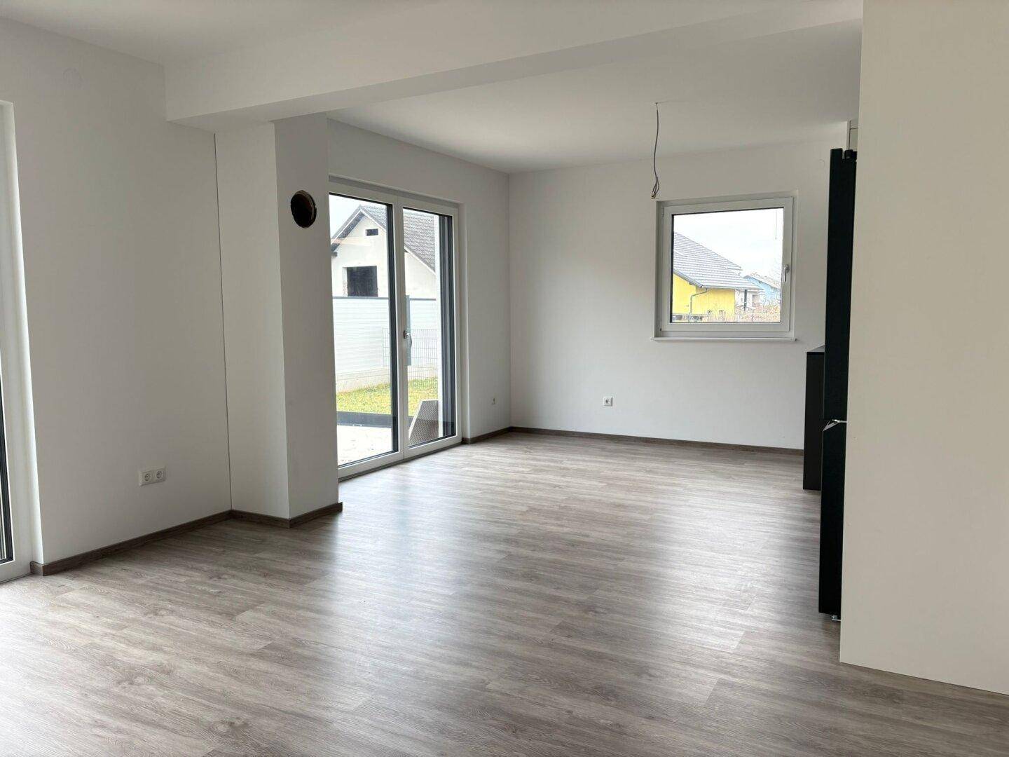 Heller Wohnbereich mit großen Schiebetüren zum Garten und einem weiteren Fenster.