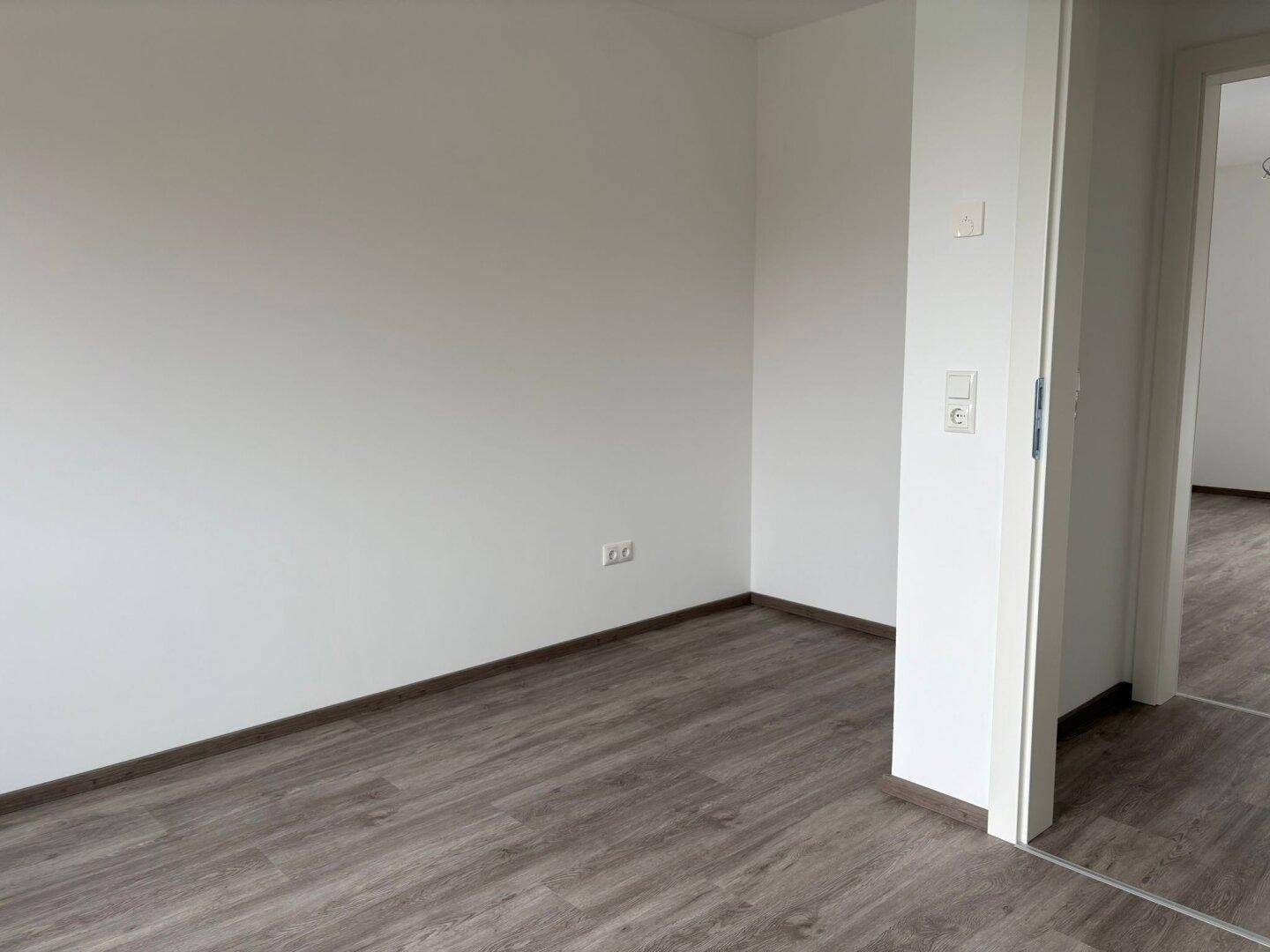 Unmöblierter Raum mit weiß gestrichenen Wänden und modernem Laminatboden.