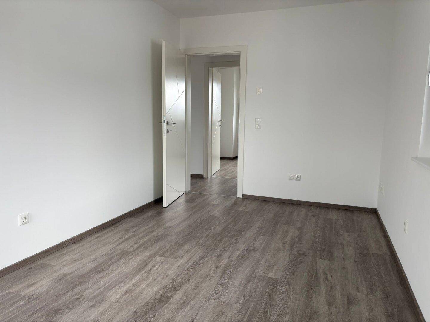 Leerer Raum mit Laminatboden und offenen Türen, die zu weiteren Zimmern führen.