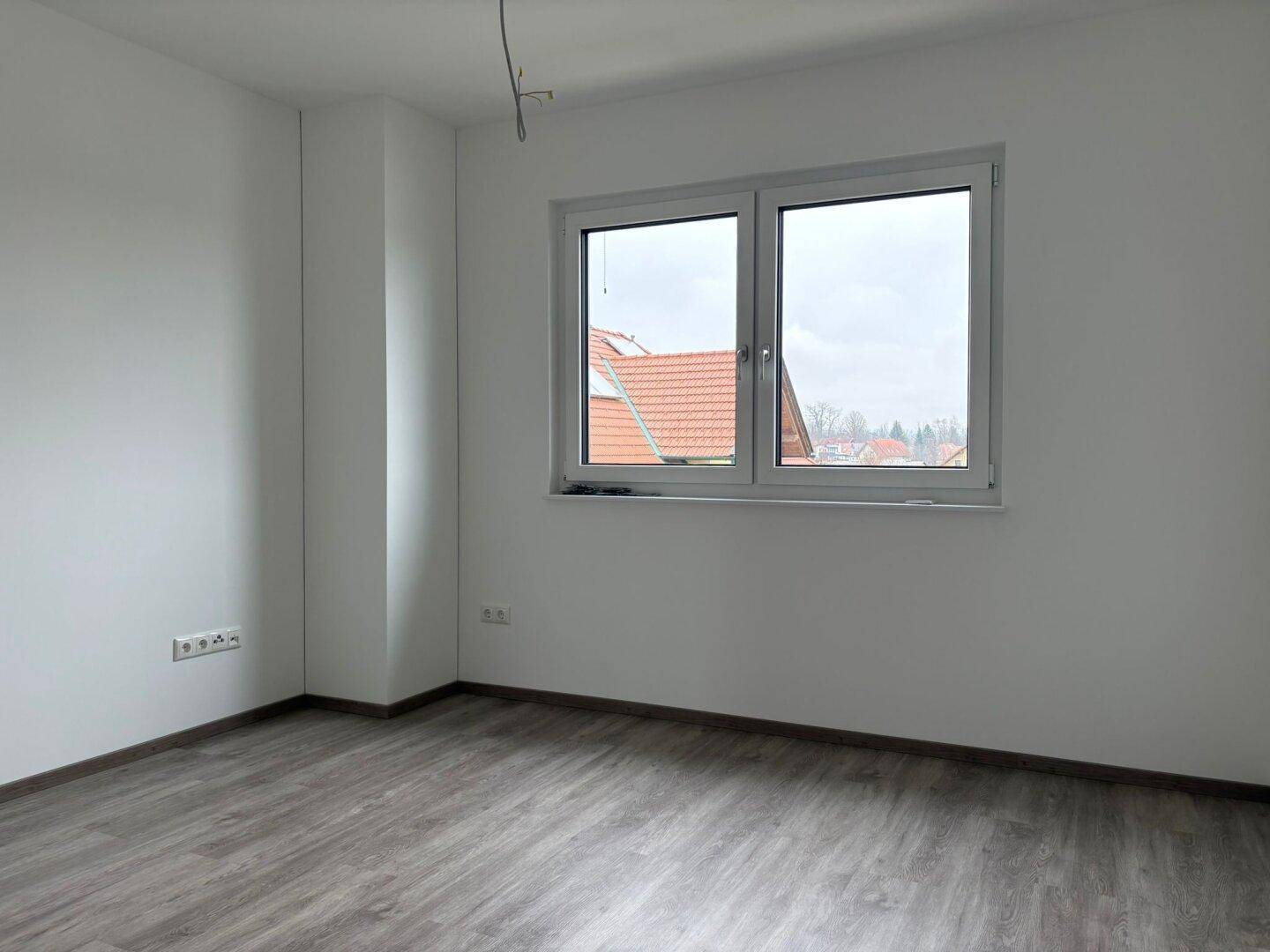 Helles Schlafzimmer mit großem Fenster und Blick auf die Dächer der Nachbarschaft.