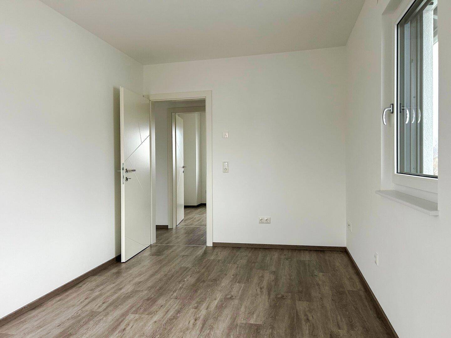 Helles Schlafzimmer mit Laminatboden und weiß gestrichenen Wänden.