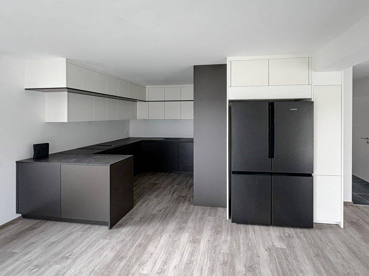 Moderne Küche mit schwarzen und weißen Schränken sowie großem Kühlschrank.