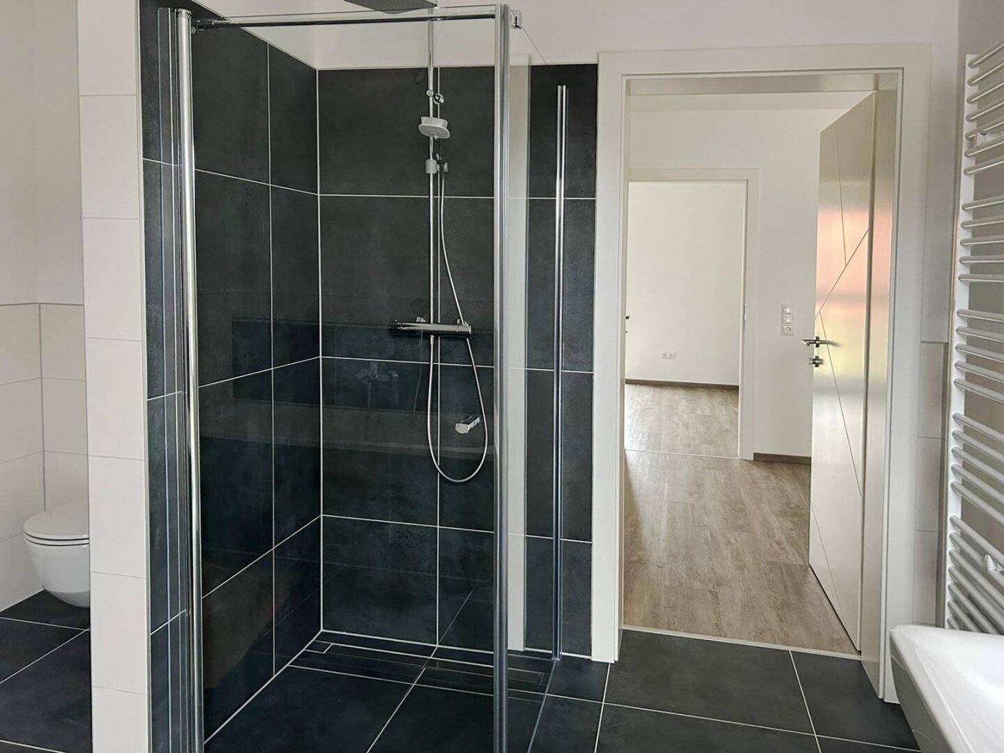 Modernes Badezimmer mit großer Duschkabine und dunklen Fliesen.