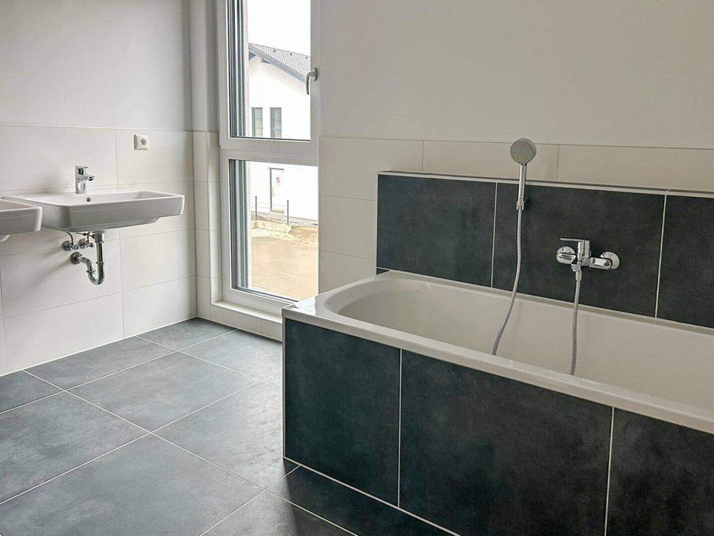 Helles Badezimmer mit Badewanne, Einzelwaschbecken und Fenster.