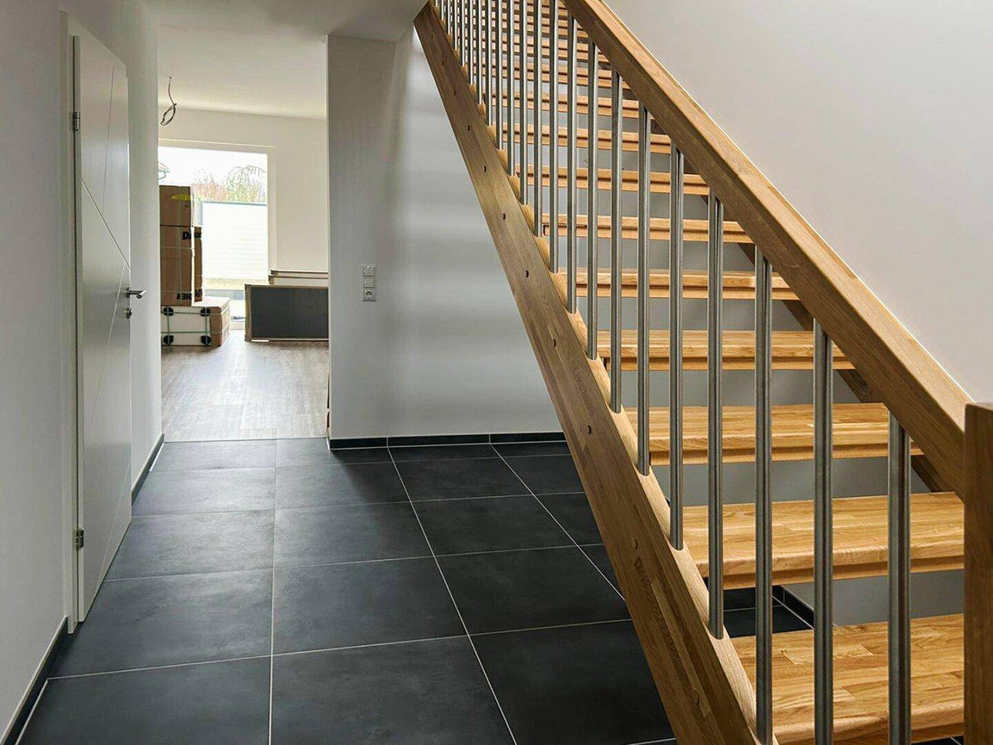 Eingangsbereich mit moderner Holztreppe und dunklen Fliesen.