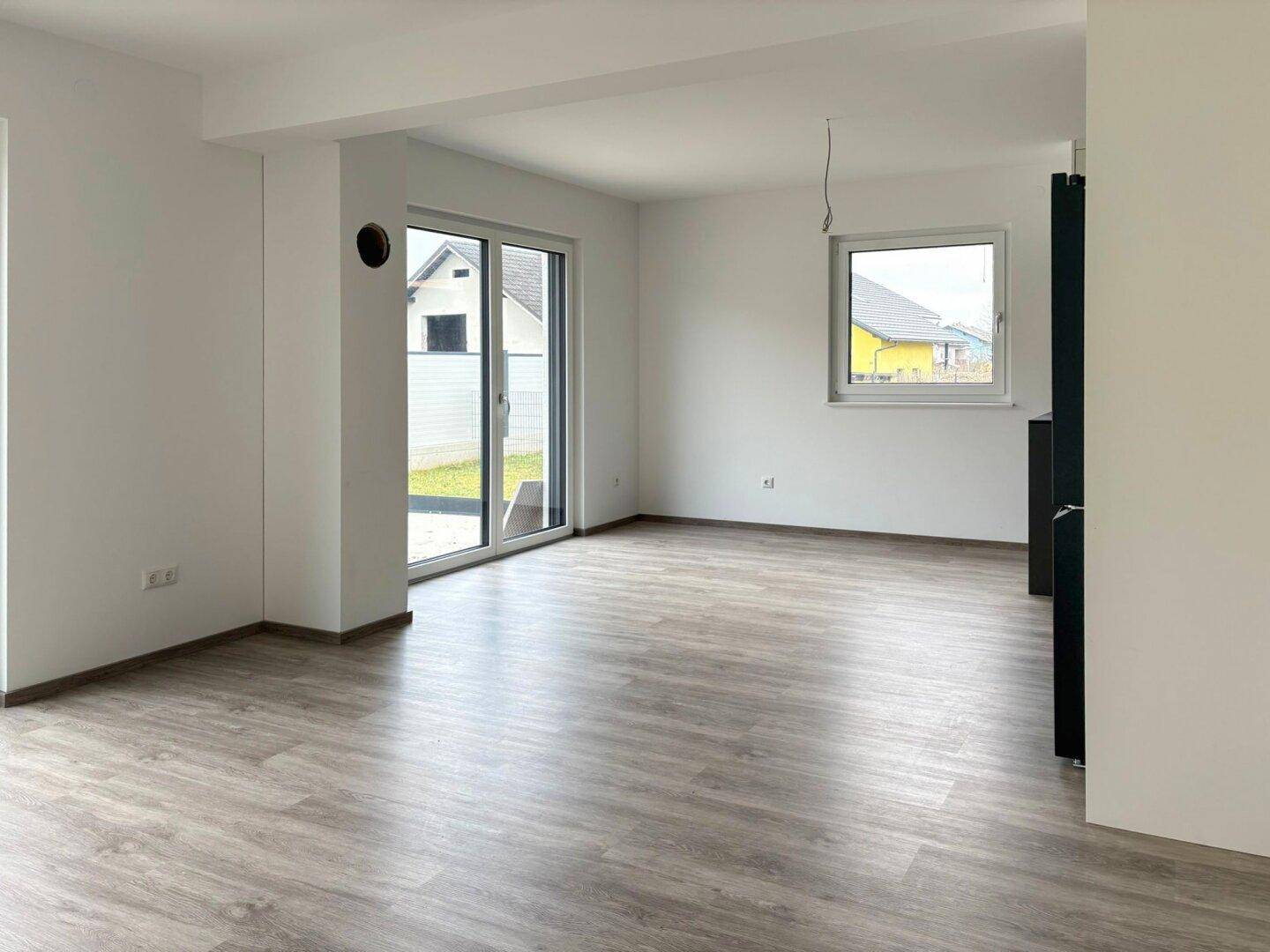 Heller Wohnbereich mit Laminatboden und Zugang zur Terrasse durch große Schiebetüren.