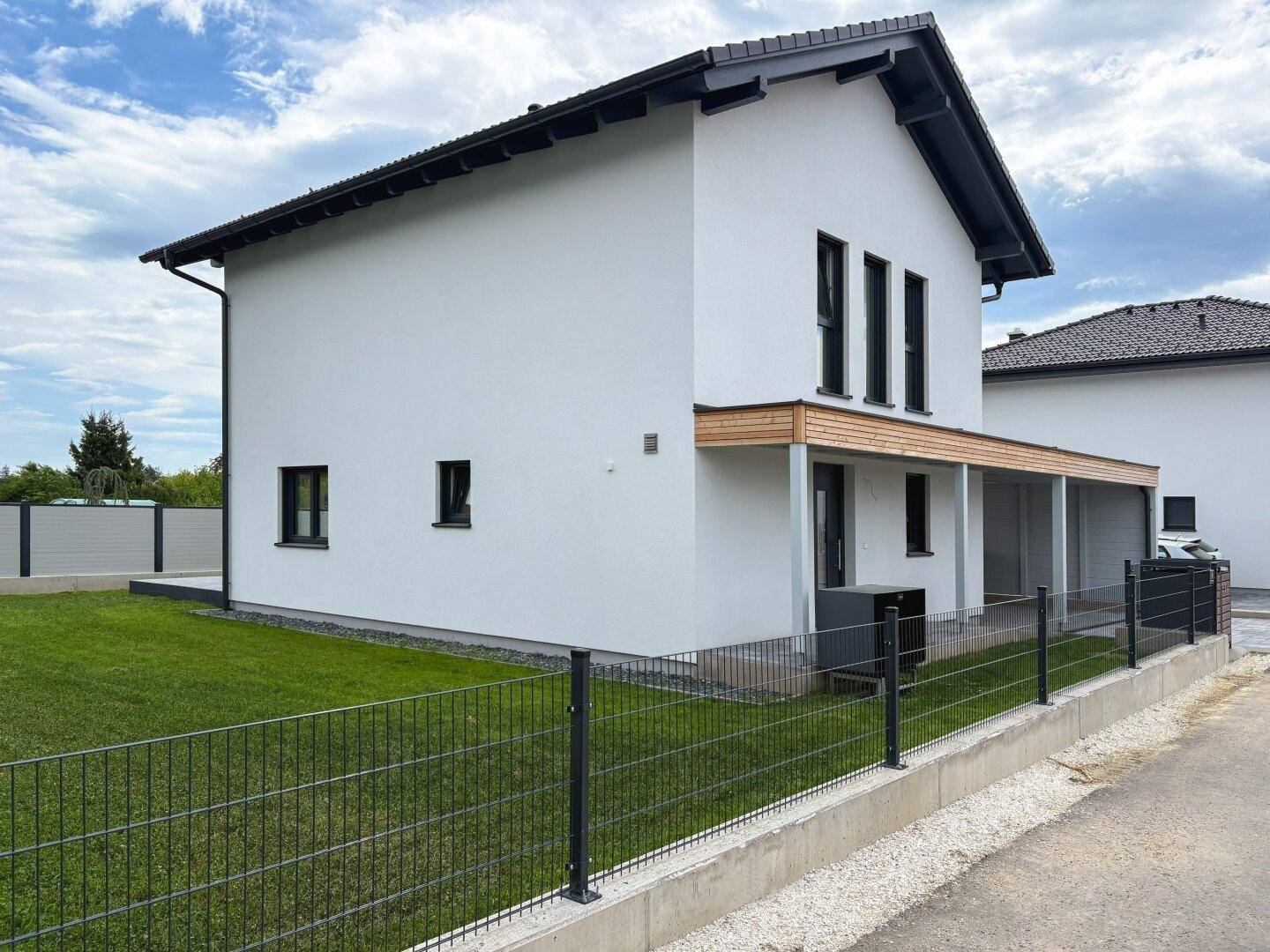 Seitenansicht des Neubaus mit gepflegtem Rasen und Zaun.