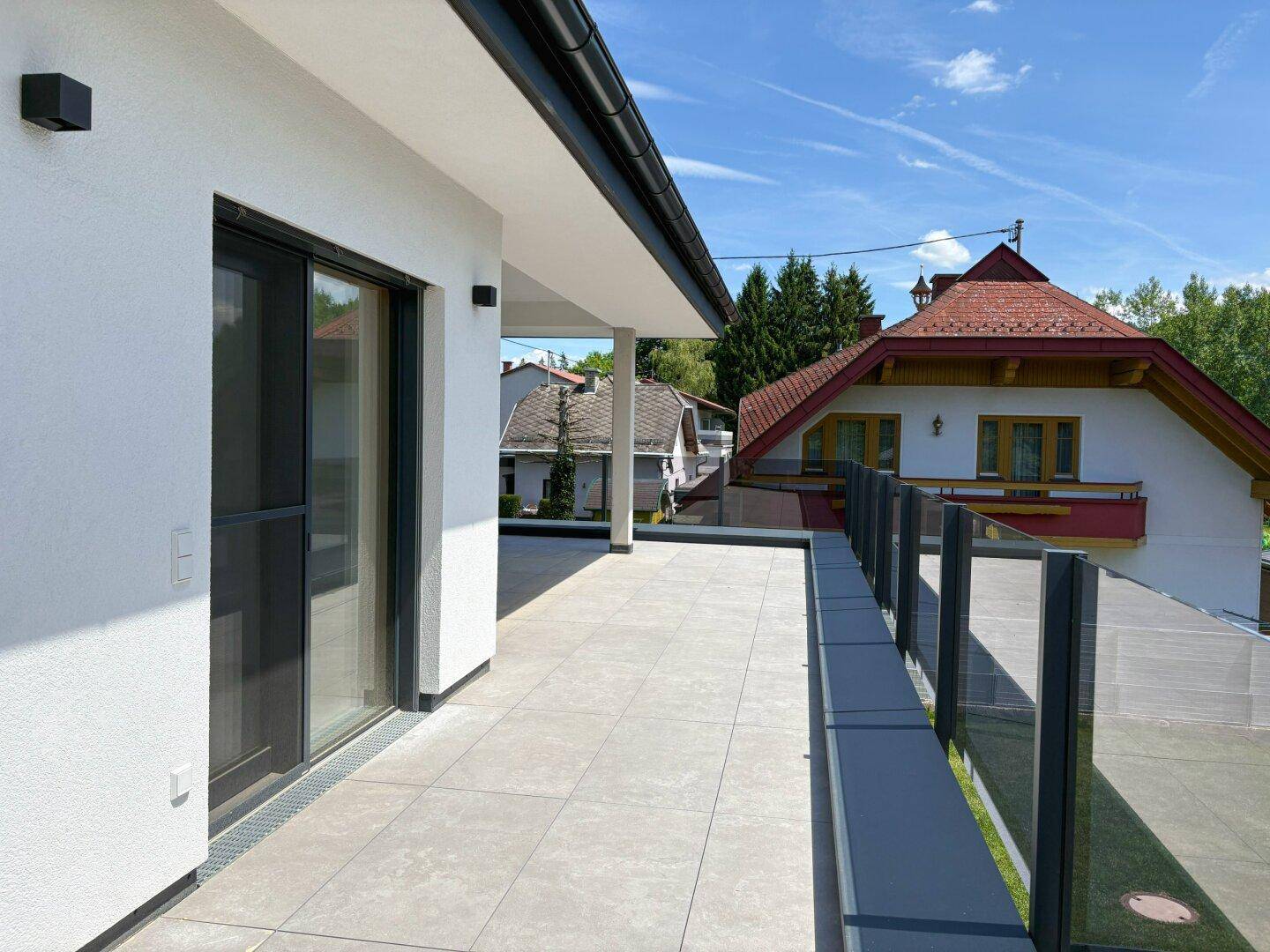 Moderne Terrasse mit Glasgeländer und Blick auf die Nachbarschaft unter blauem Himmel.