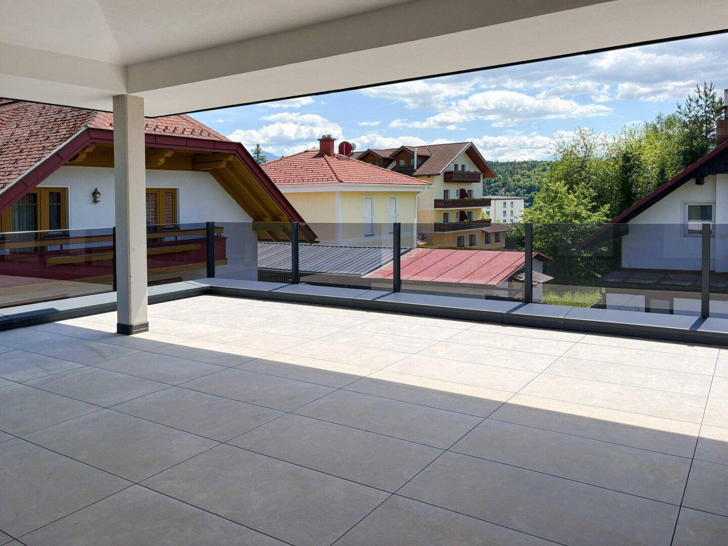 Weitläufige Terrasse mit Glasgeländer und Blick auf die umliegenden Häuser und grüne Landschaft.