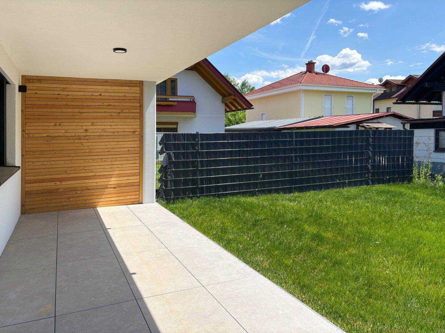 Überdachte Terrasse mit Holzverkleidung und Zugang zum privaten Gartenbereich.