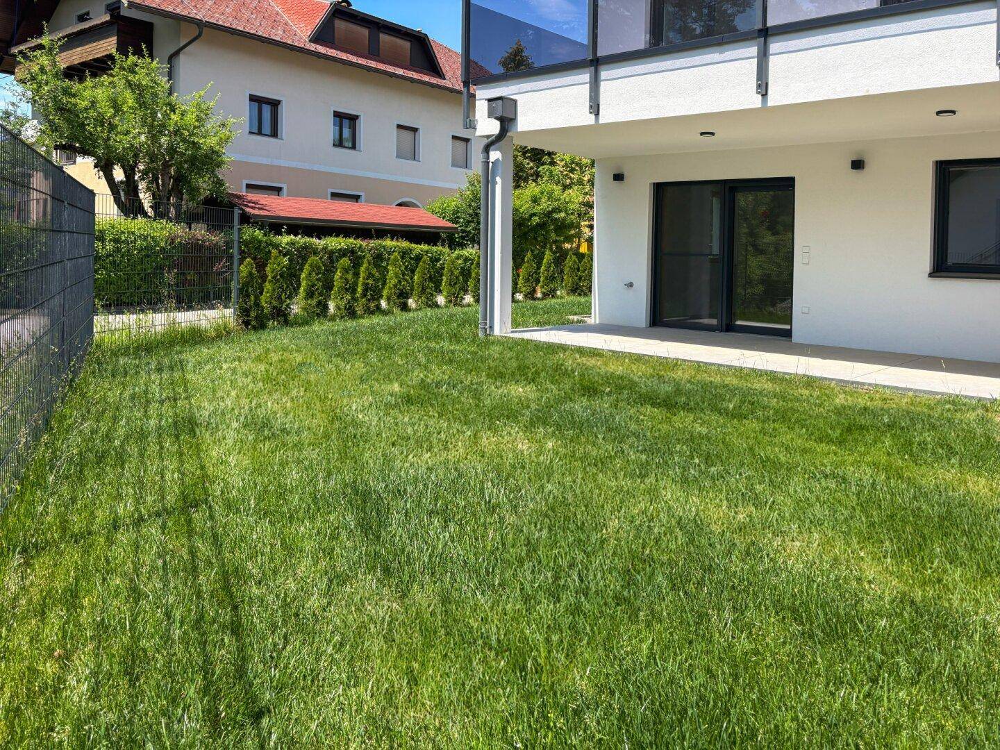 Gepflegter Rasenbereich mit Blick auf die Terrasse und das moderne Gebäude.