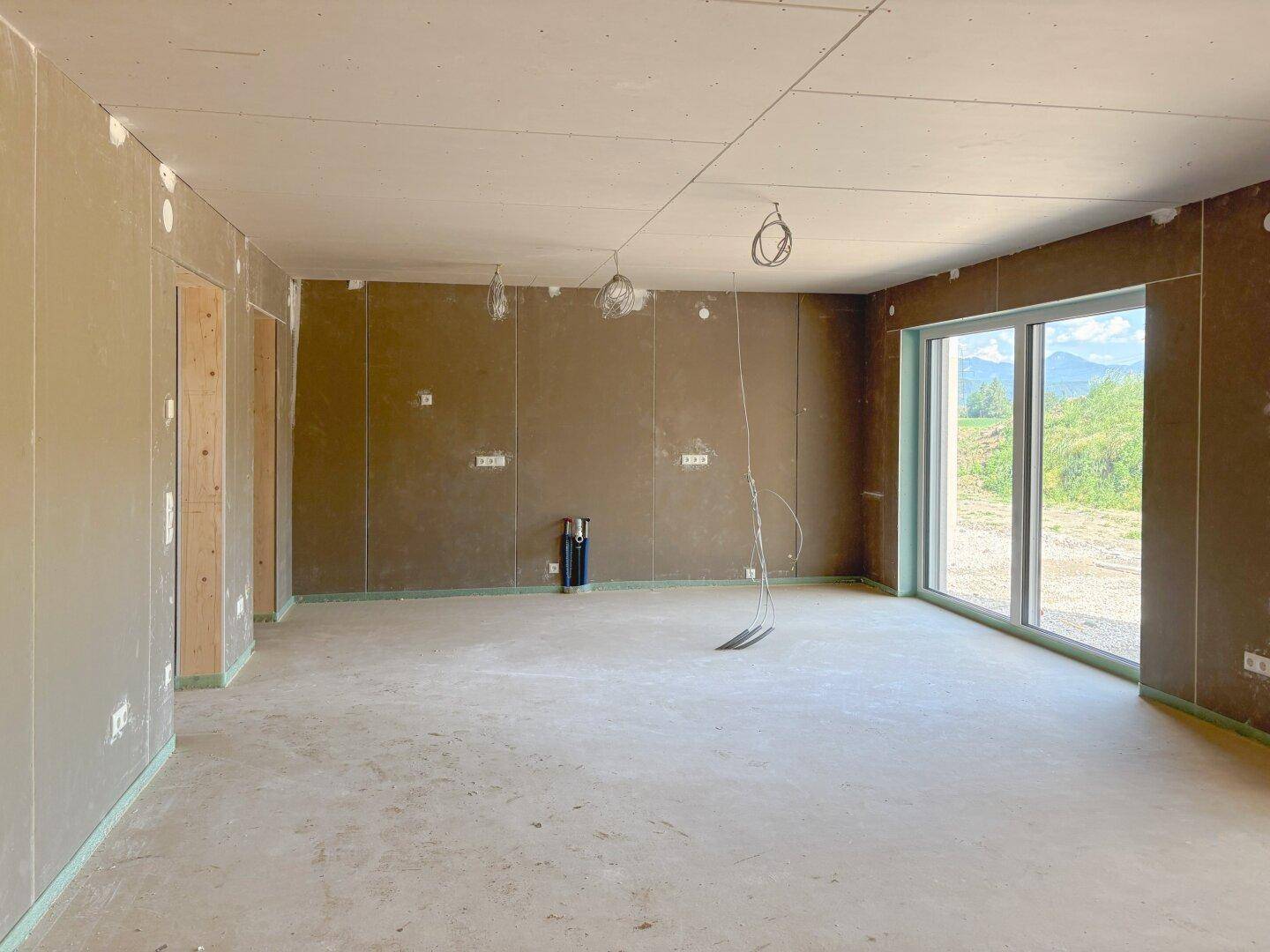 Geräumiger Wohnbereich im Rohbau mit großen Schiebetüren und Blick ins Grüne.