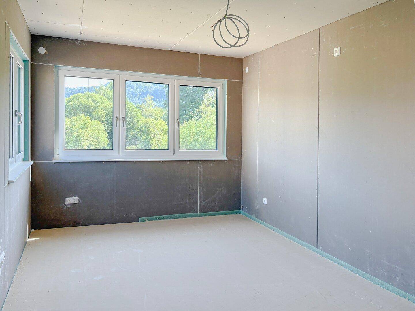 Helles Zimmer im Rohbau mit Fenster und Ausblick auf die umliegende Natur.