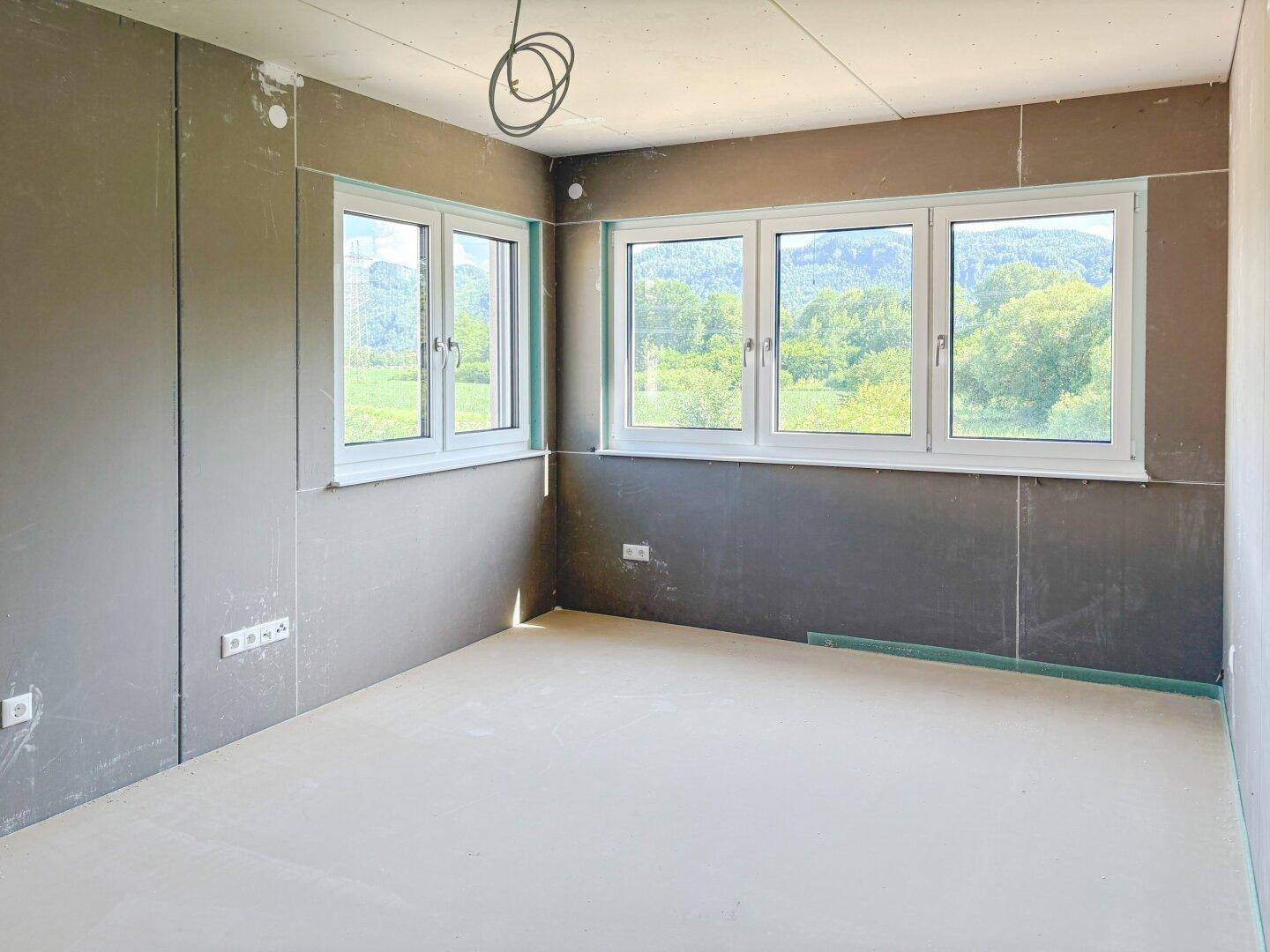 Eckzimmer im Rohbau mit zwei Fenstern und weitem Blick auf die Landschaft.
