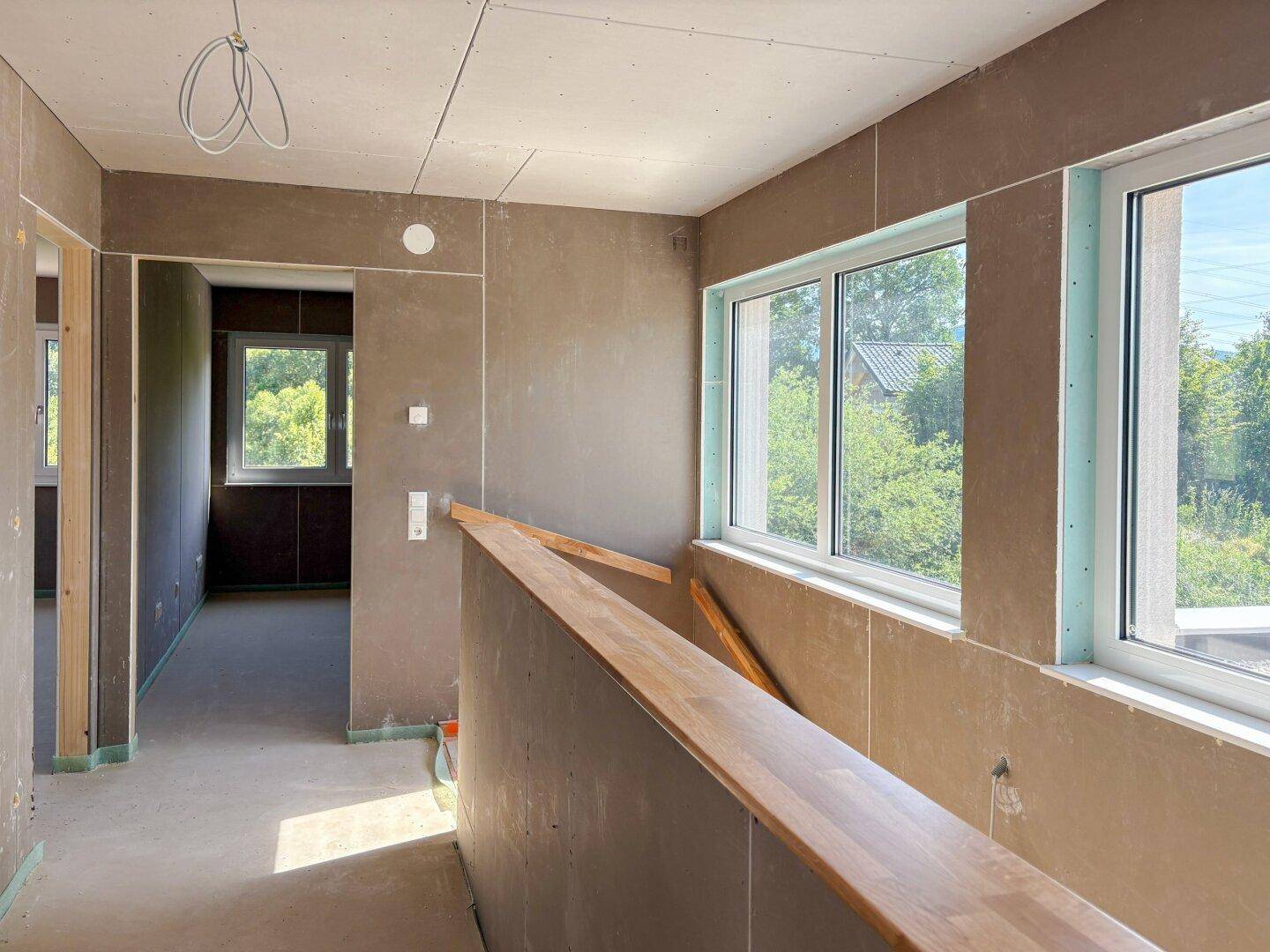 Heller Flur im Obergeschoss mit Holzgeländer und Fenstern mit Blick ins Grüne.