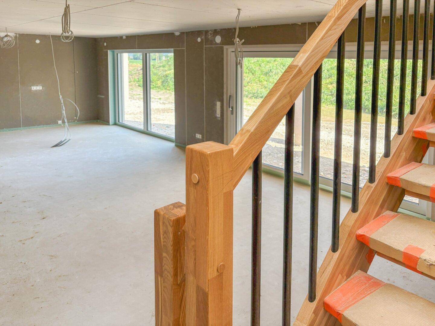 Detailansicht der Holztreppe mit Blick auf den offenen Wohnbereich im Rohbau.