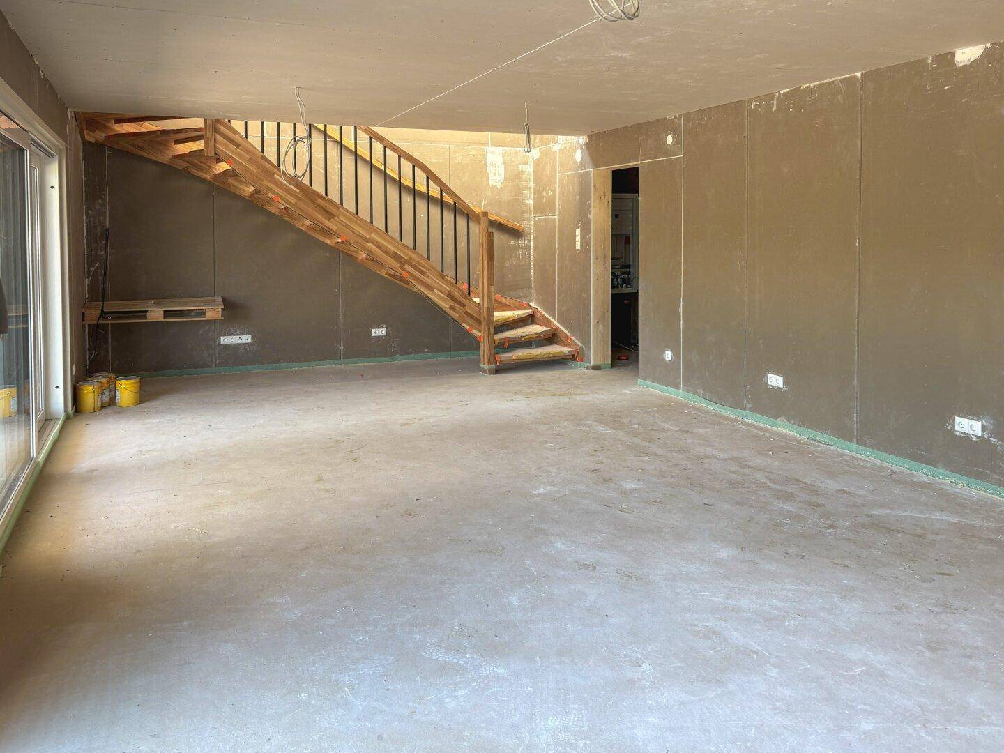 Geräumiger Wohnbereich im Rohbau mit Holztreppe und viel Potenzial zur Gestaltung.
