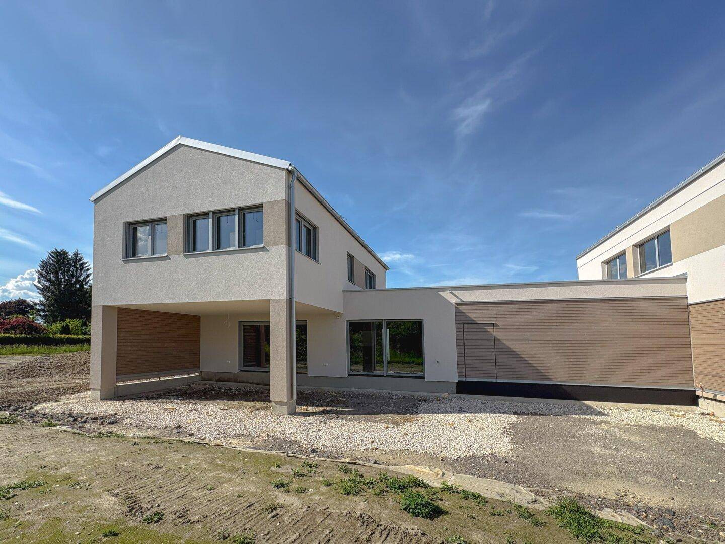 Neubau-Doppelhaushälfte mit Carport und moderner Architektur in ländlicher Umgebung.