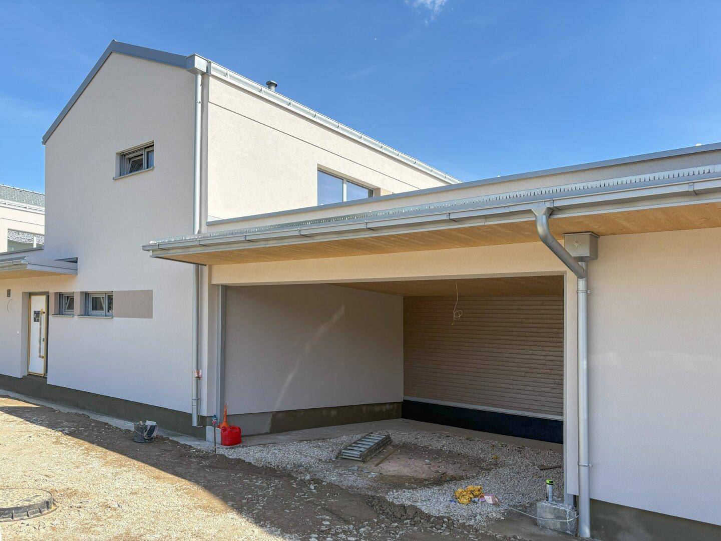 Seitenansicht des Neubaus mit überdachtem Carport und moderner Fassade.