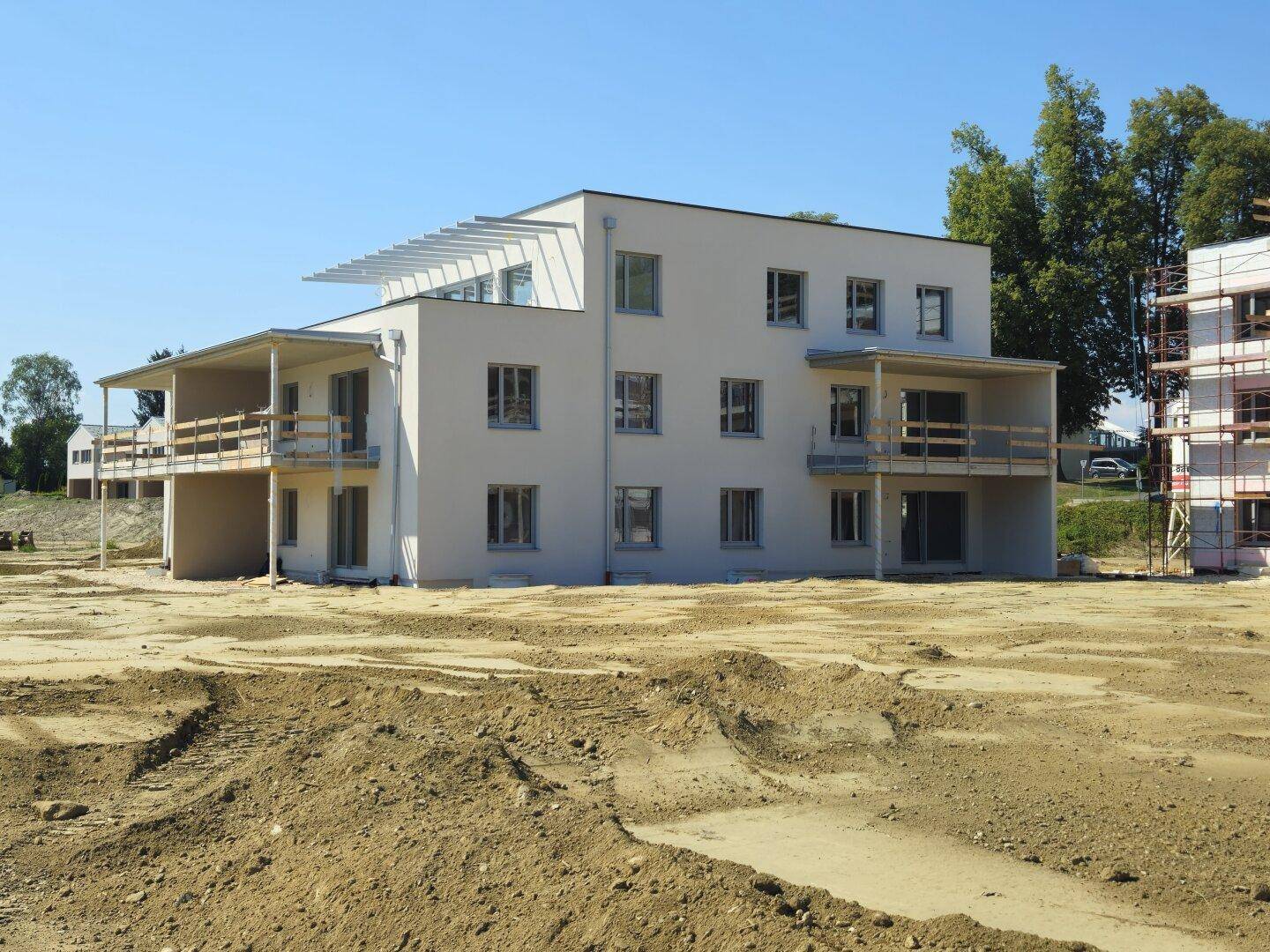 Neubau eines Mehrfamilienhauses mit mehreren Balkonen auf einem weitläufigen Baugrundstück.