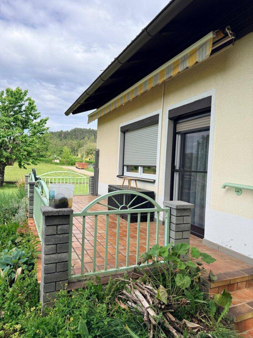 Kleine geflieste Terrasse am Haus mit Metallgeländer, Markise und Blick ins Grüne.