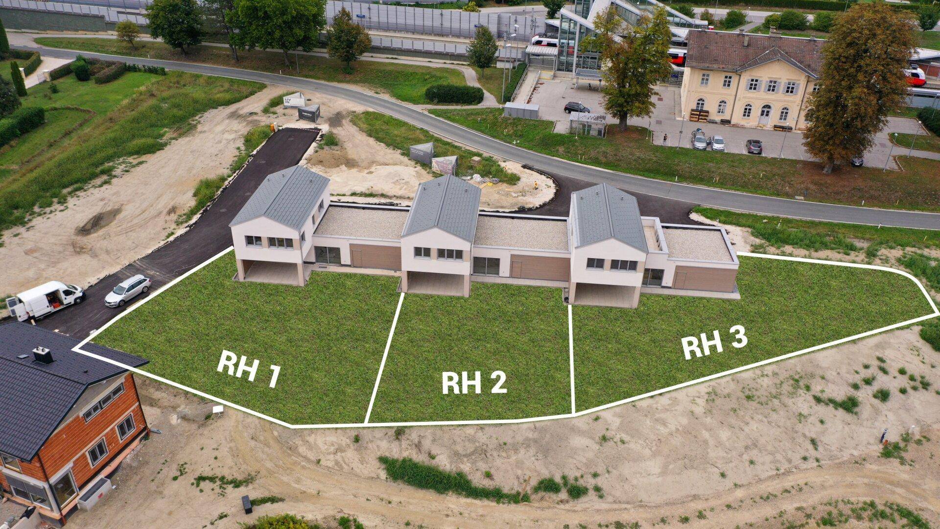 Luftaufnahme einer Neubausiedlung mit drei modernen Reihenhäusern und ihren klar abgegrenzten Gartenparzellen.