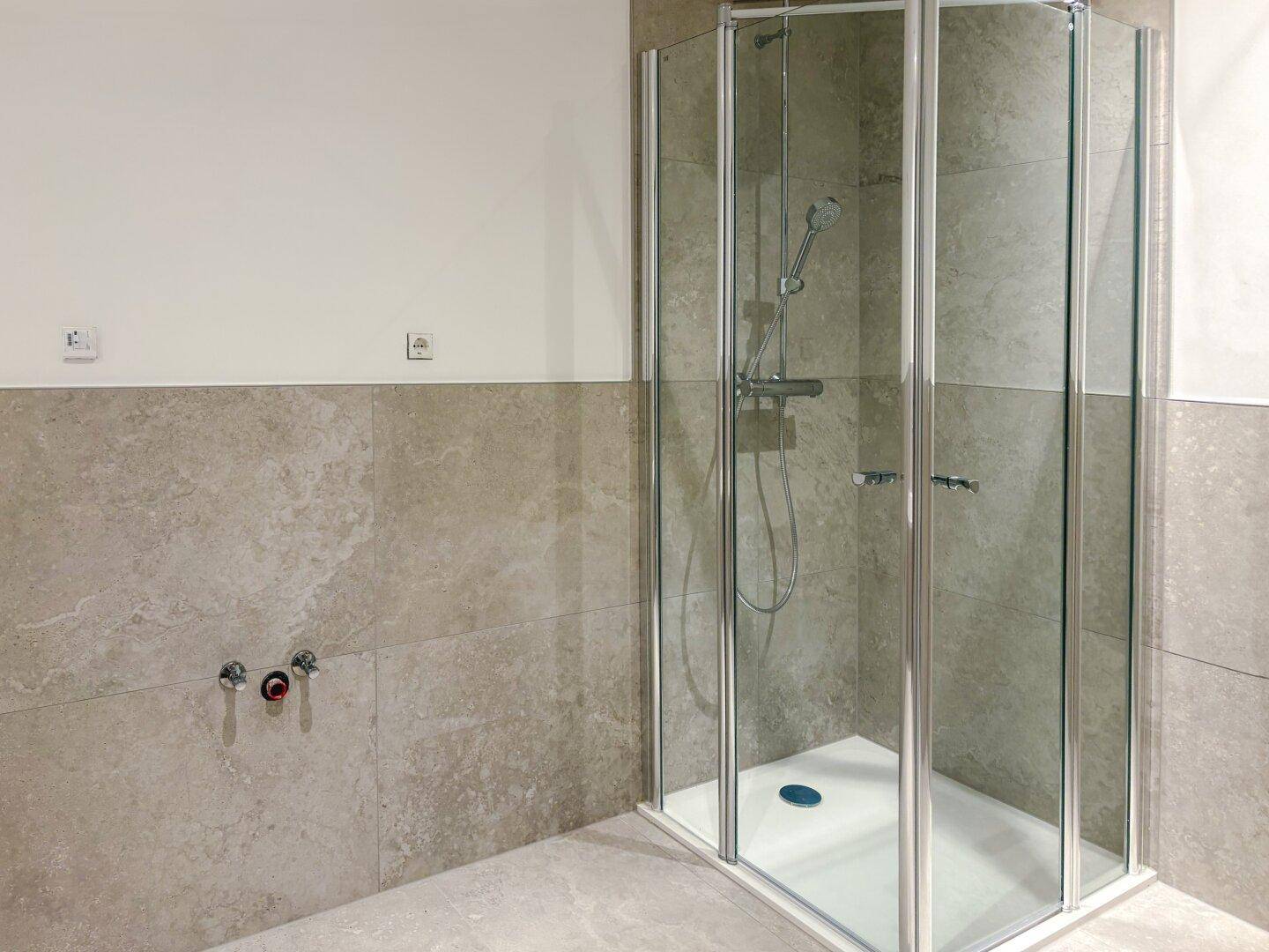 Modernes Badezimmer mit Duschkabine und hellen Fliesen an Wänden und Boden.