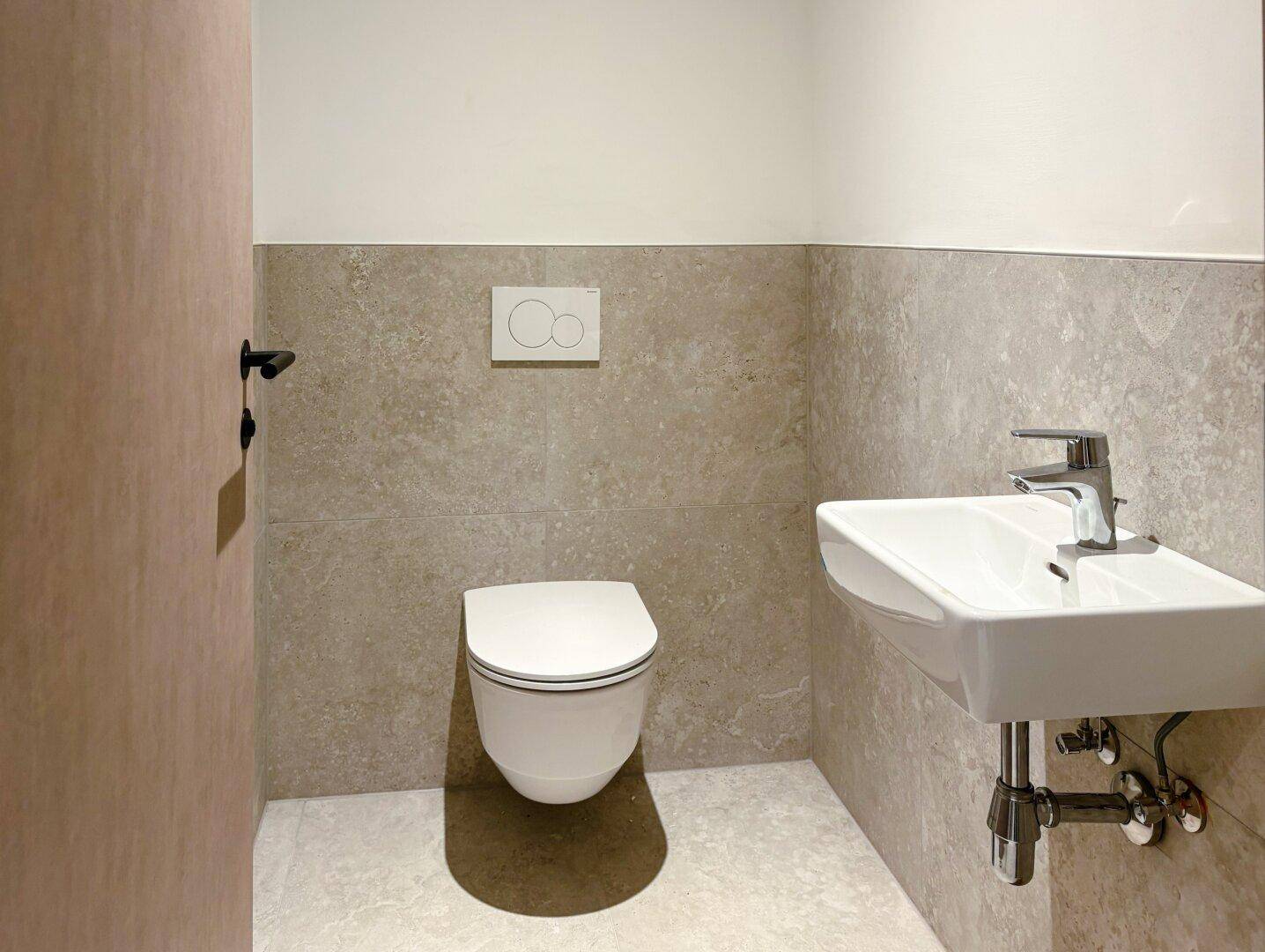 Gäste-WC mit wandhängender Toilette, kleinem Waschbecken und modernen Fliesen.