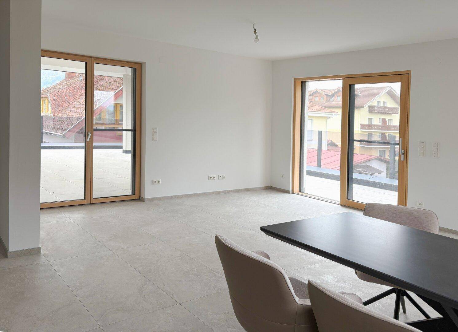 Heller, leerer Wohnbereich mit großen Fenstertüren, Fliesenboden und direktem Zugang zur Terrasse.