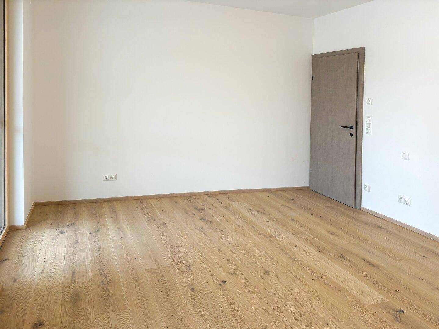Leeres Schlafzimmer mit hellem Holzparkett und weiß gestrichenen Wänden, bereit zum Einrichten.