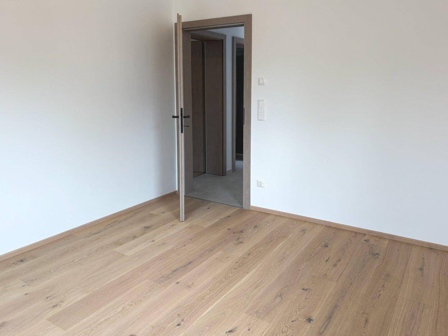 Geräumiges Schlafzimmer mit Holzboden und offener Tür, bietet Zugang zu einem weiteren Raum.
