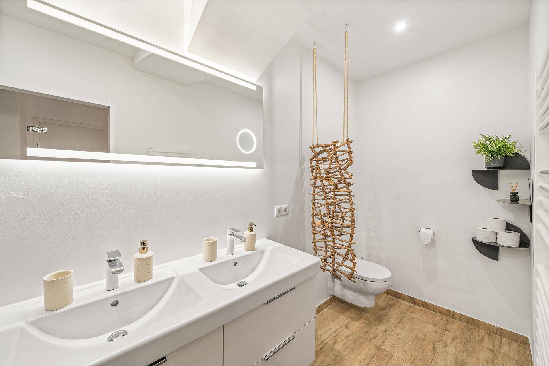 Helles Badezimmer mit Doppelwaschbecken, Wand-WC und dekorativer Holzelementen.