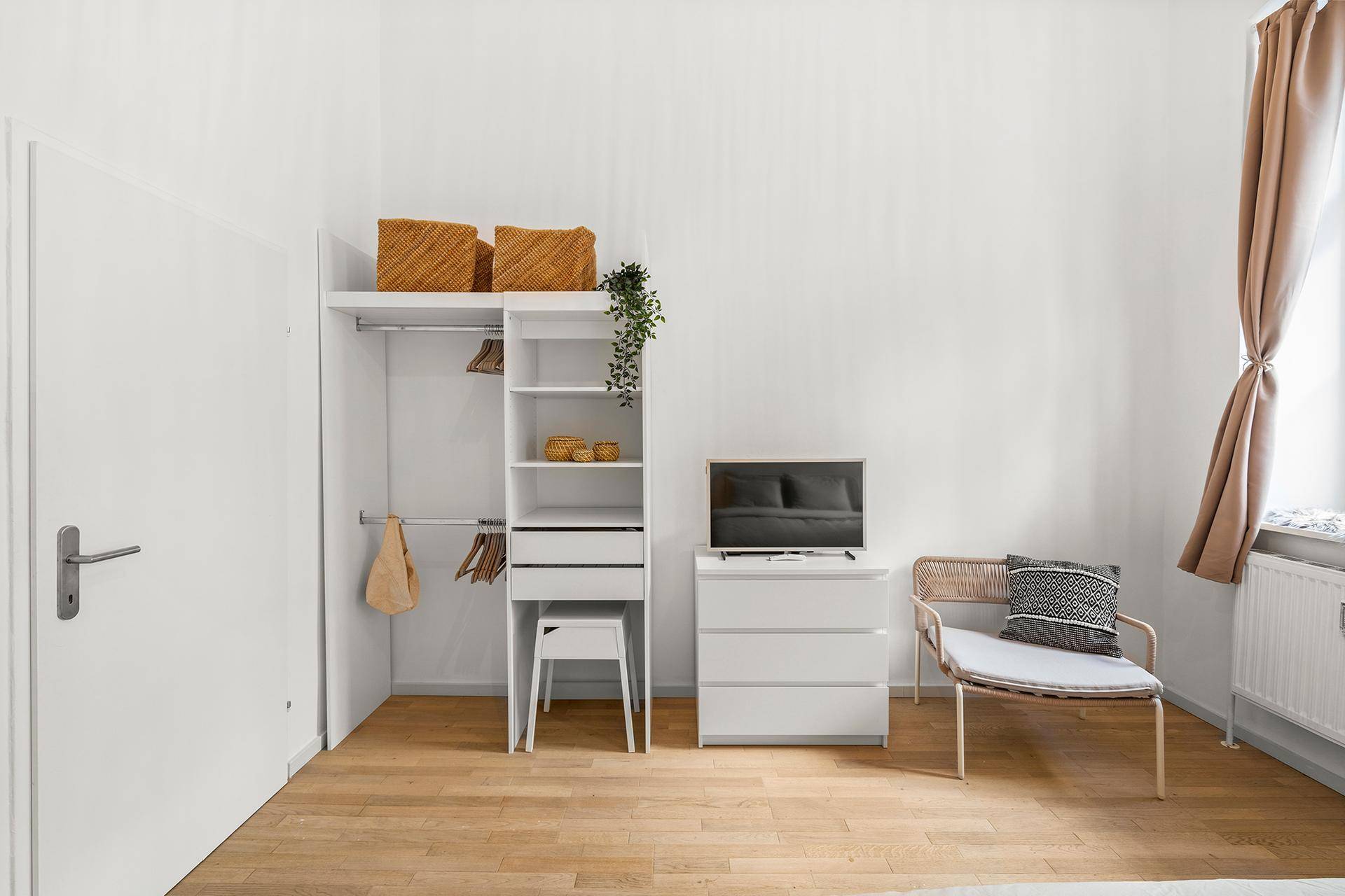 Schlafzimmer mit offenem Kleiderschrank, Kommode und Fernseher in modernem Design.
