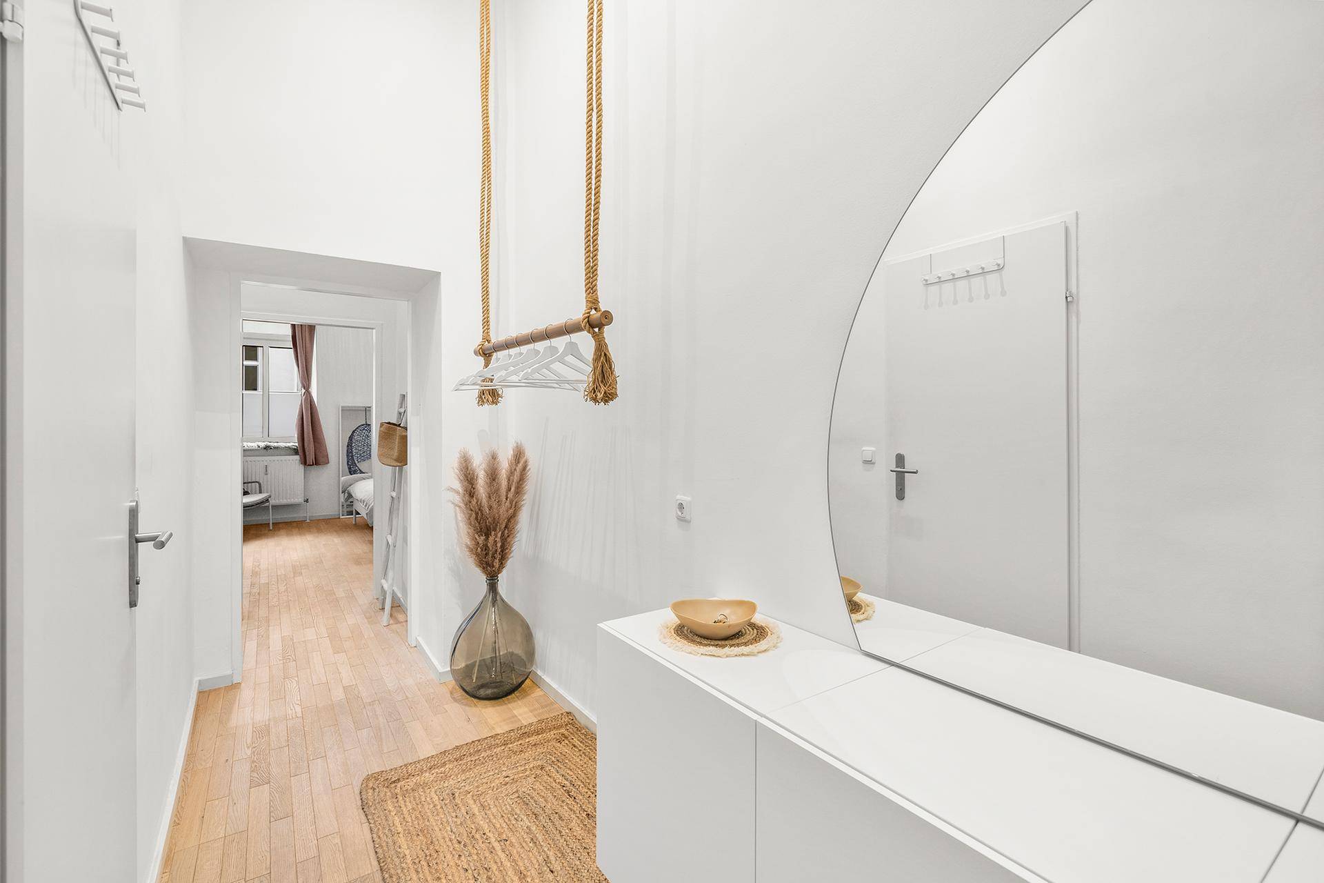 Heller Flur mit Holzboden, großem Spiegel und moderner Garderobenlösung an der Wand.