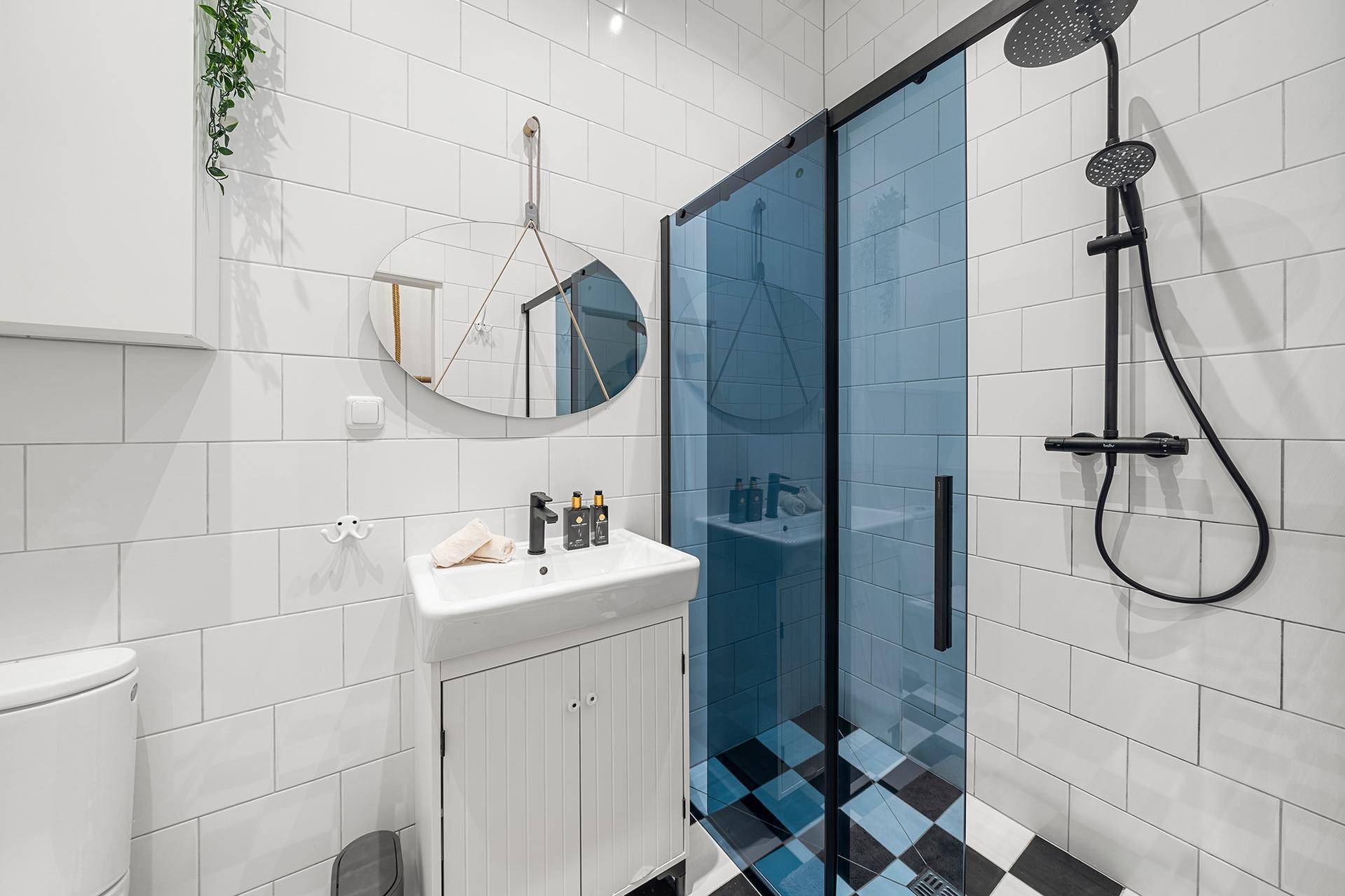Modernes Badezimmer mit weiß gefliesten Wänden und einer begehbaren Dusche mit blauer Glaswand.