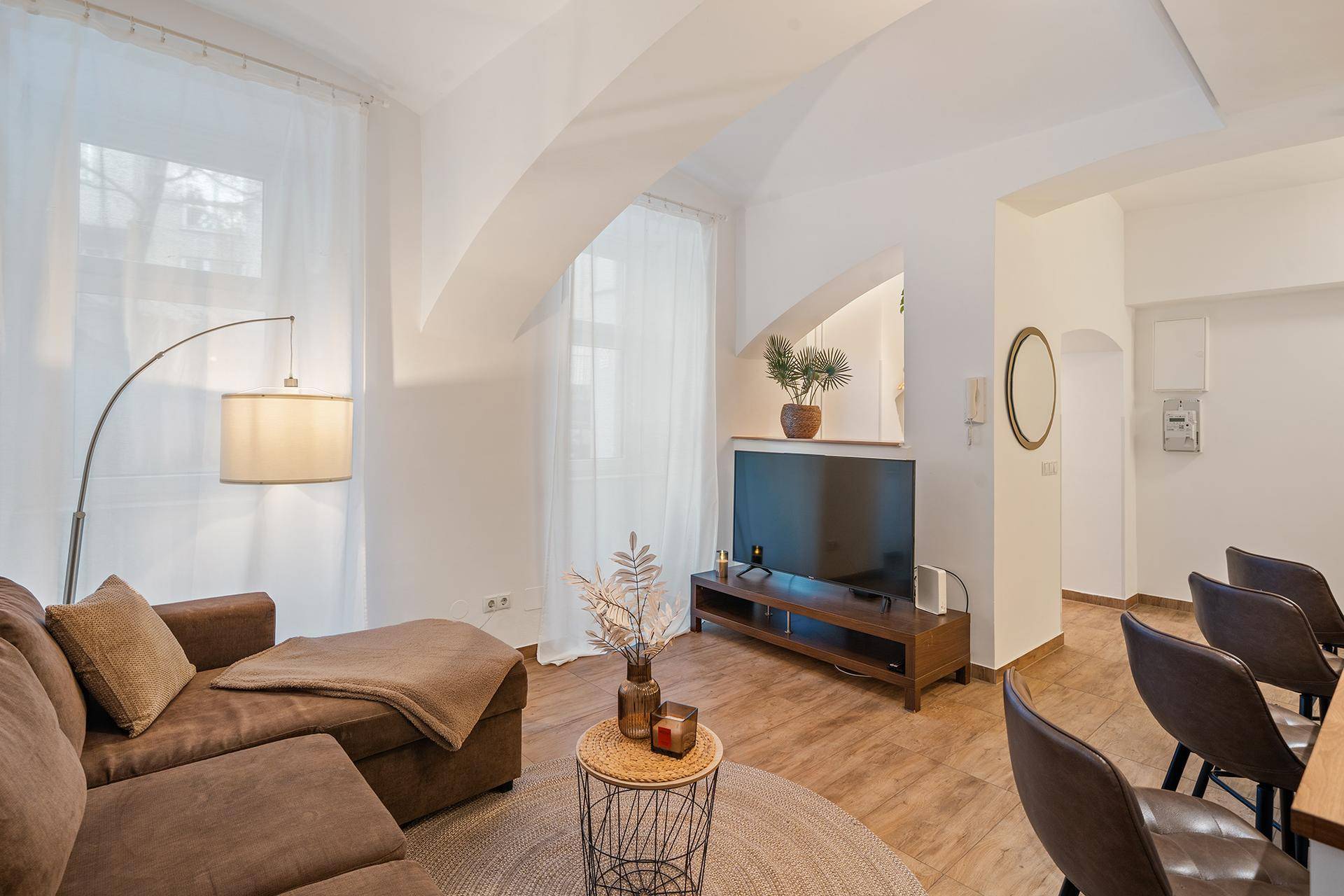 Gemütlicher Wohnbereich mit braunem Ecksofa, Fernseher und großen Fenstern.