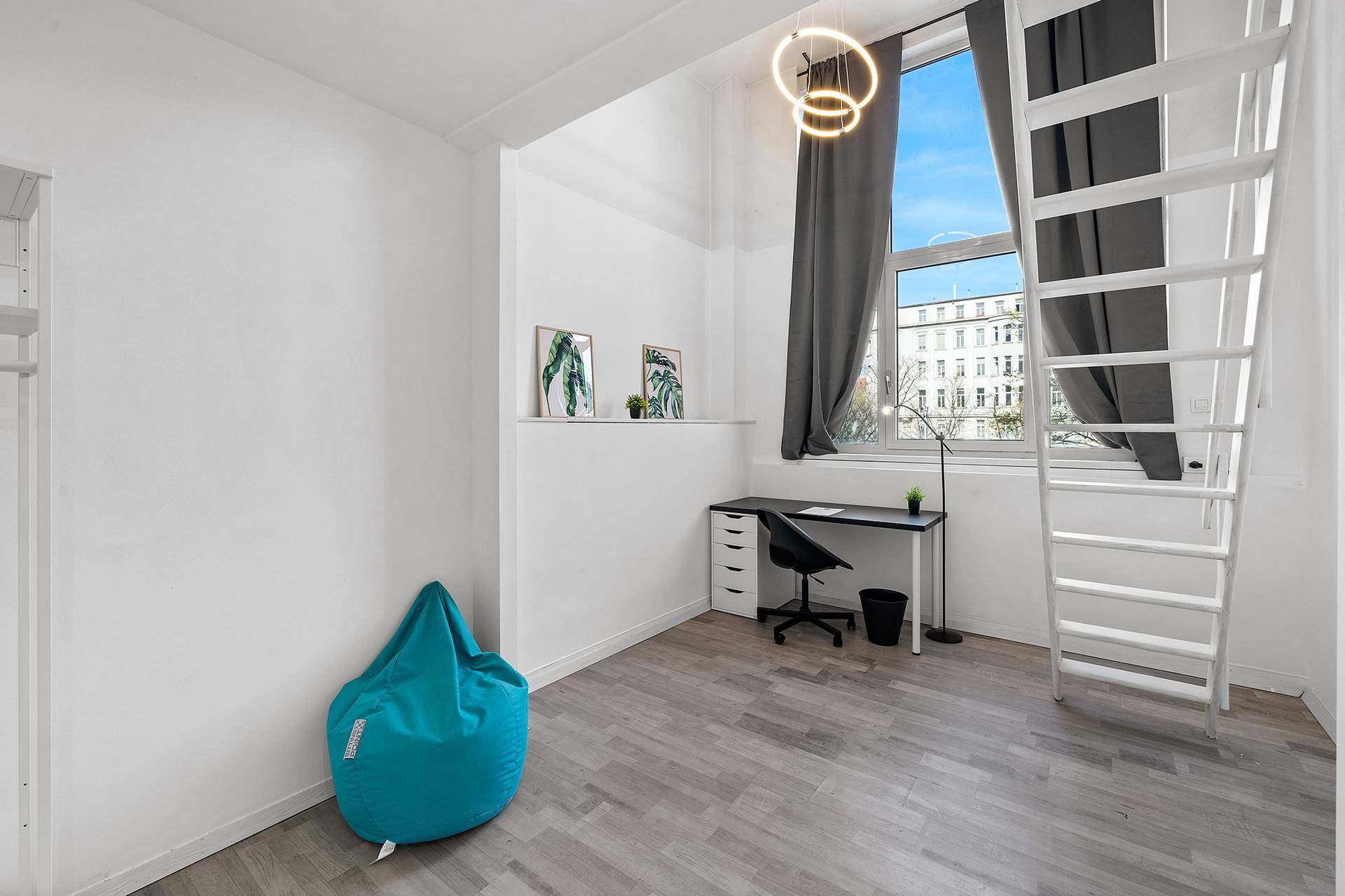 Helles Zimmer mit Schreibtisch, Sitzsack und Zugang zu einer erhöhten Schlafebene.