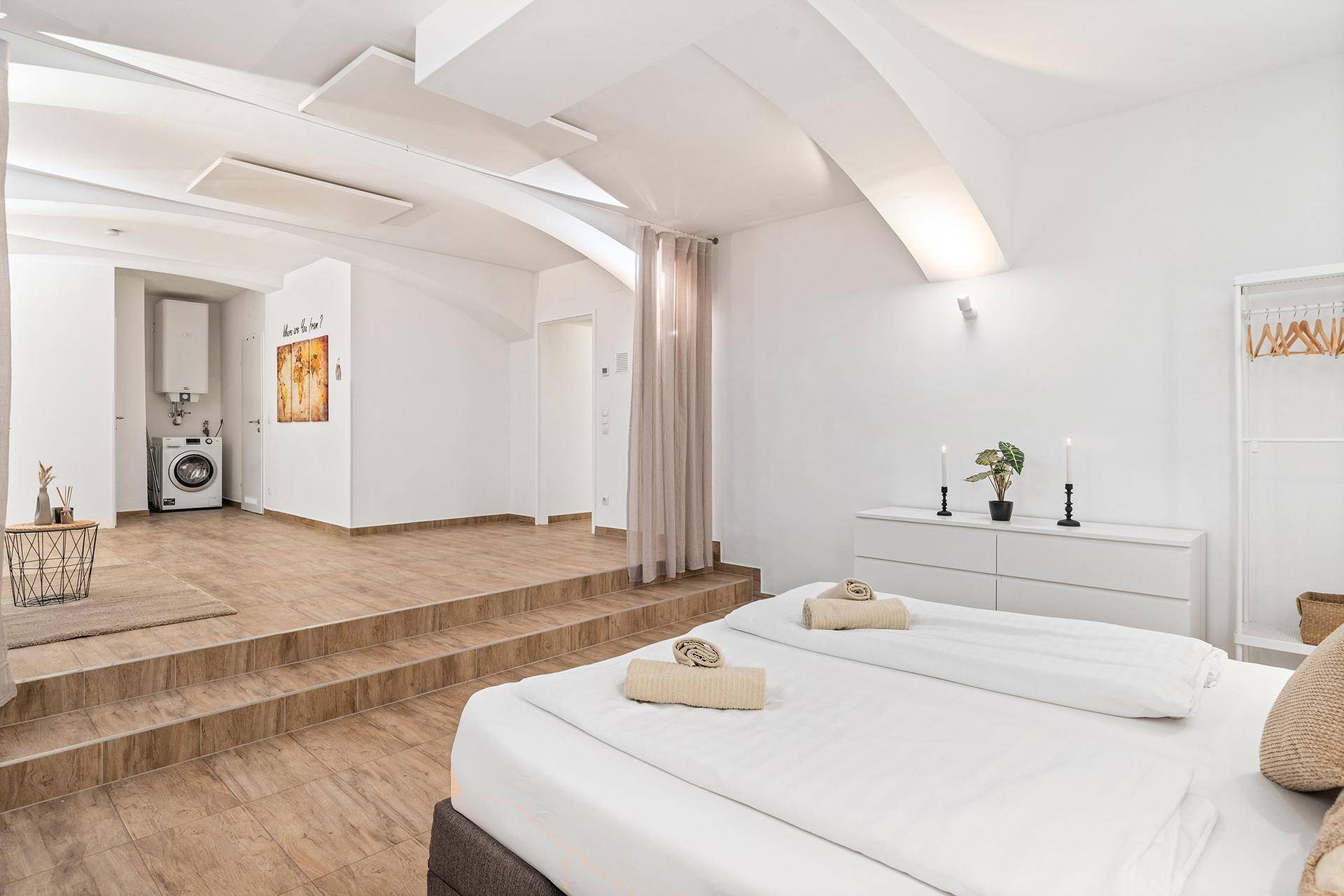 Schlafzimmer mit Doppelbett und Blick auf einen erhöhten Bereich mit Waschmaschine.