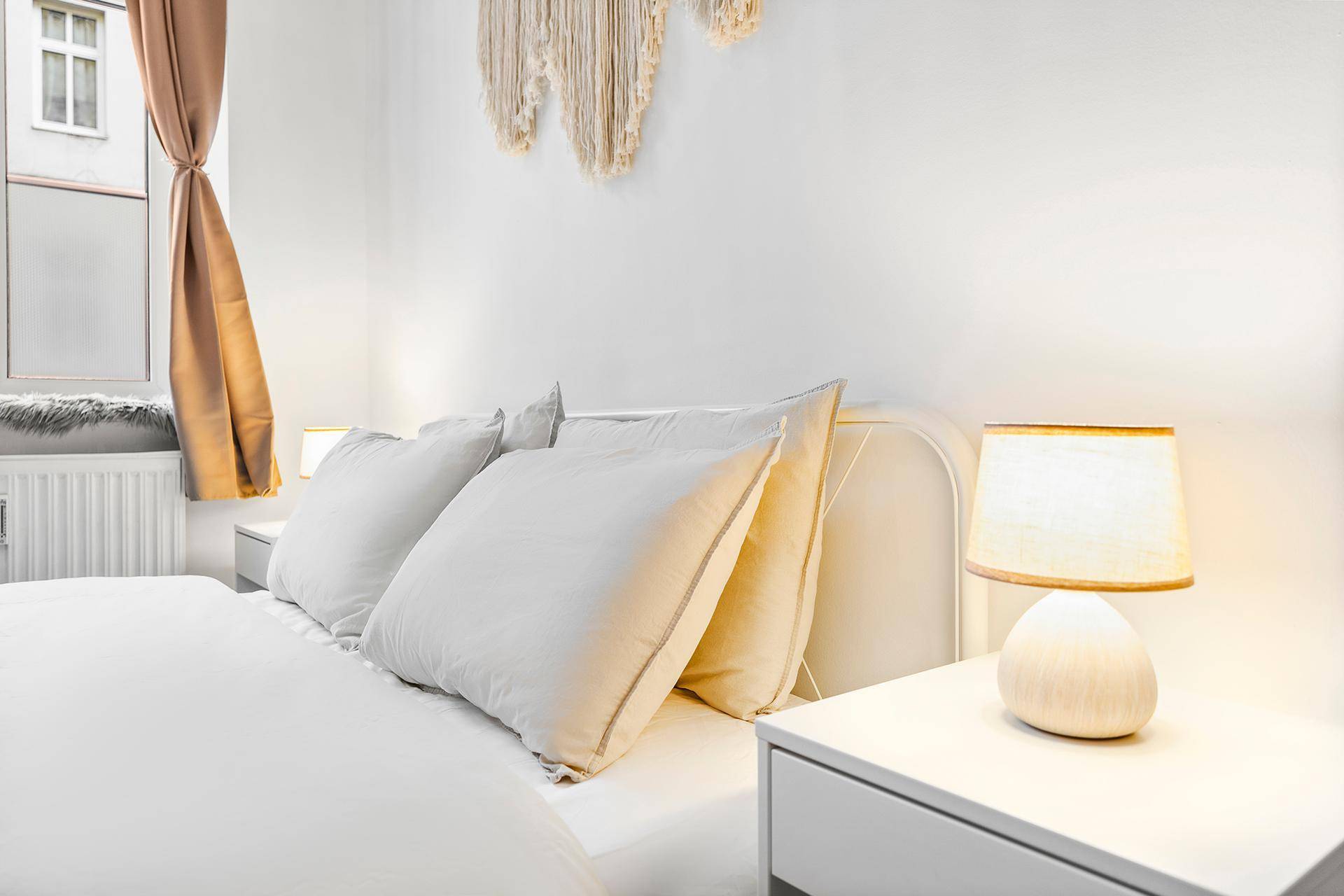 Nahaufnahme des Bettes mit Nachttisch und Lampe in einem hellen Schlafzimmer.