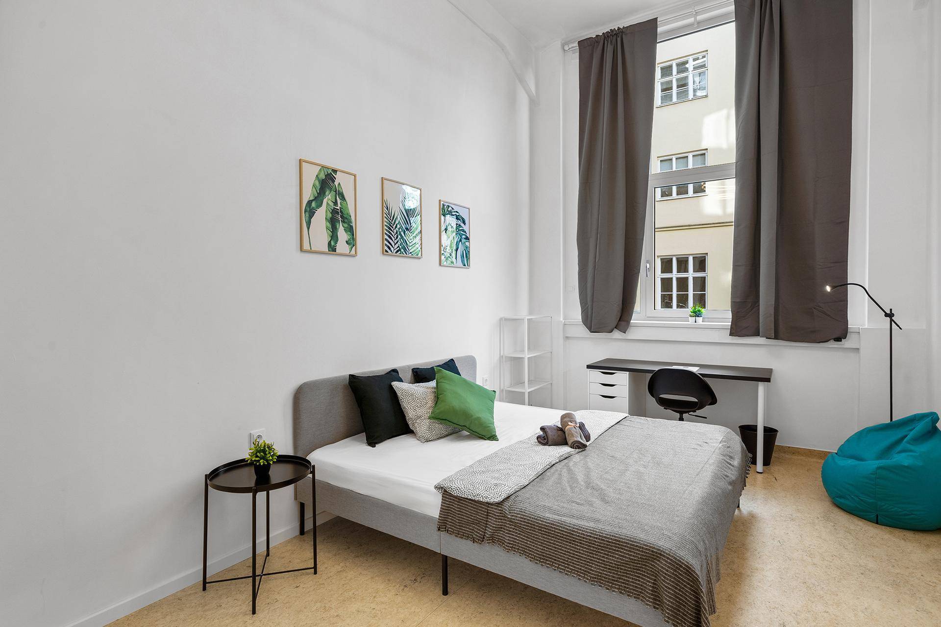 Helles Schlafzimmer mit Bett, Schreibtisch und Blick auf die Stadt.