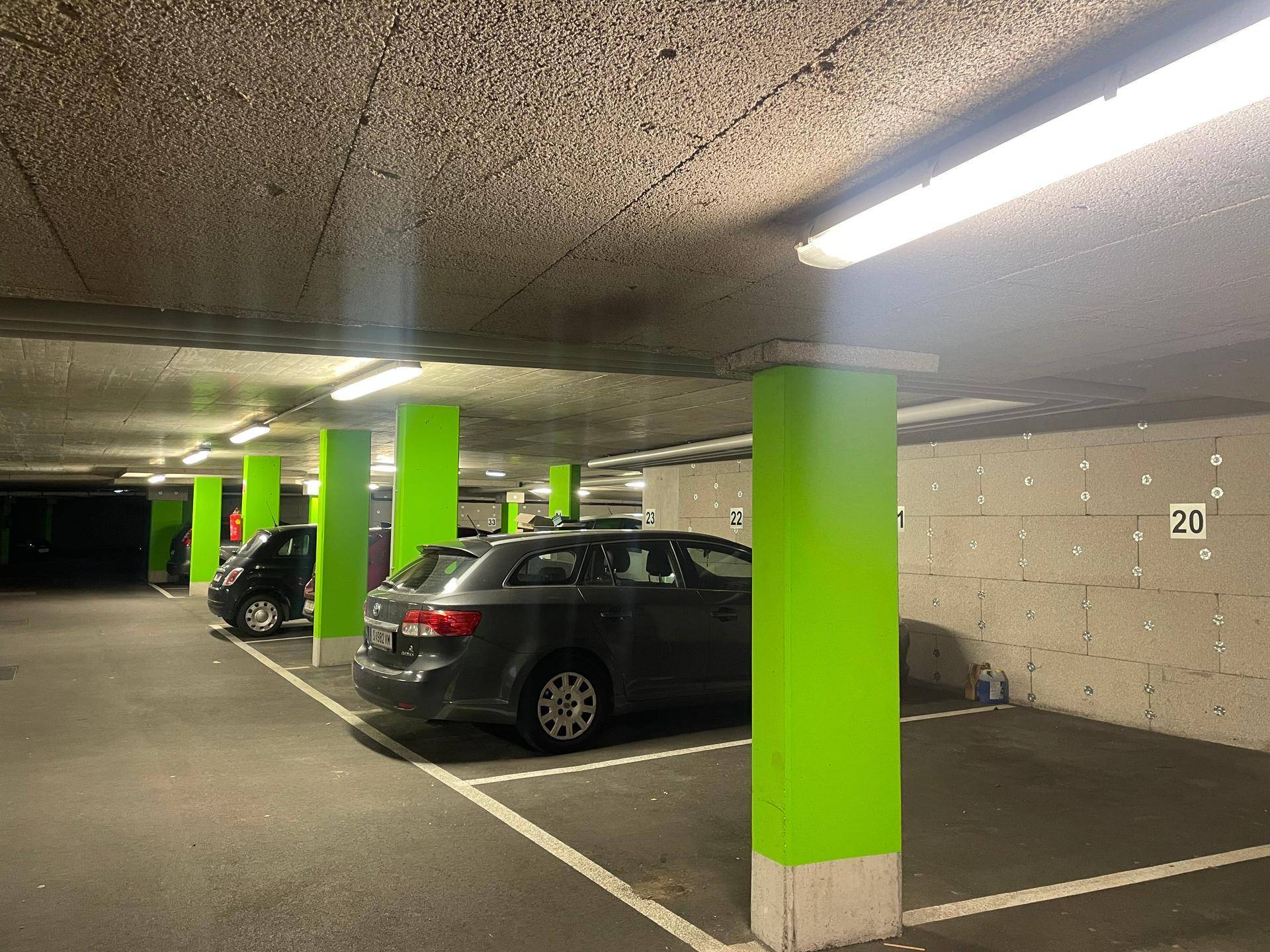 Geräumige Tiefgarage mit mehreren Stellplätzen, Betonwänden und markanten grünen Säulen.