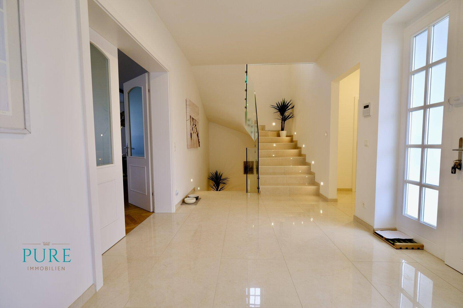 Heller Eingangsbereich mit glänzenden Fliesen, moderner Treppe und indirekter Beleuchtung.