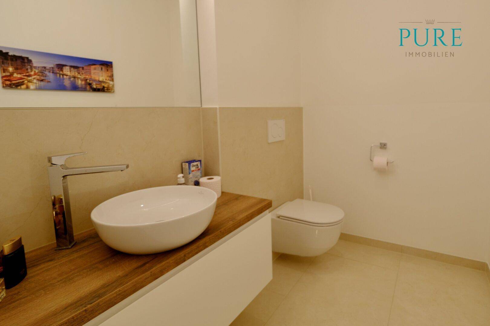 Modernes Gäste-WC mit Aufsatzwaschbecken, Holzplatte und Wand-WC.
