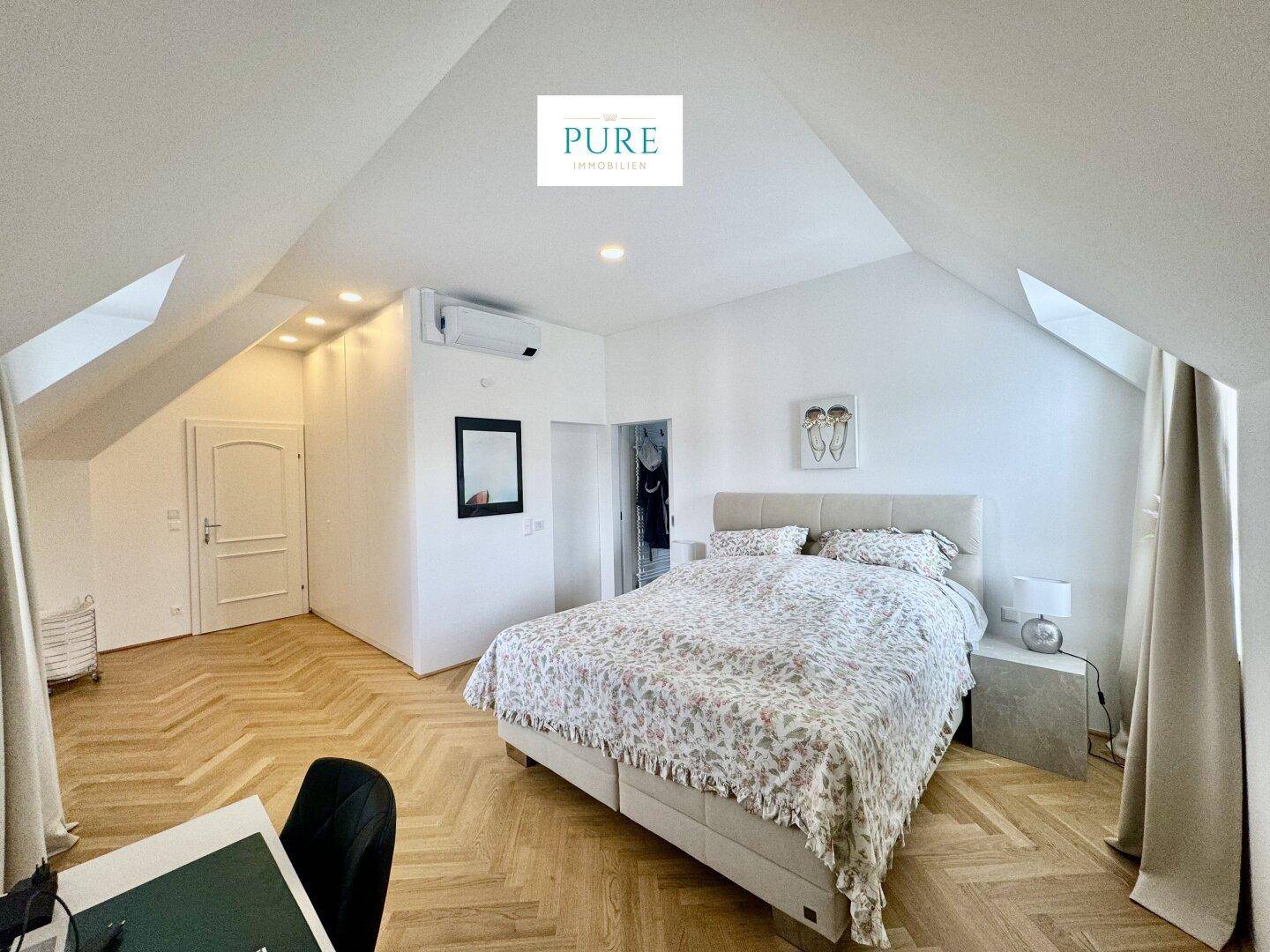 Helles Schlafzimmer im Dachgeschoss mit Parkettboden, Klimaanlage und schrägen Wänden.