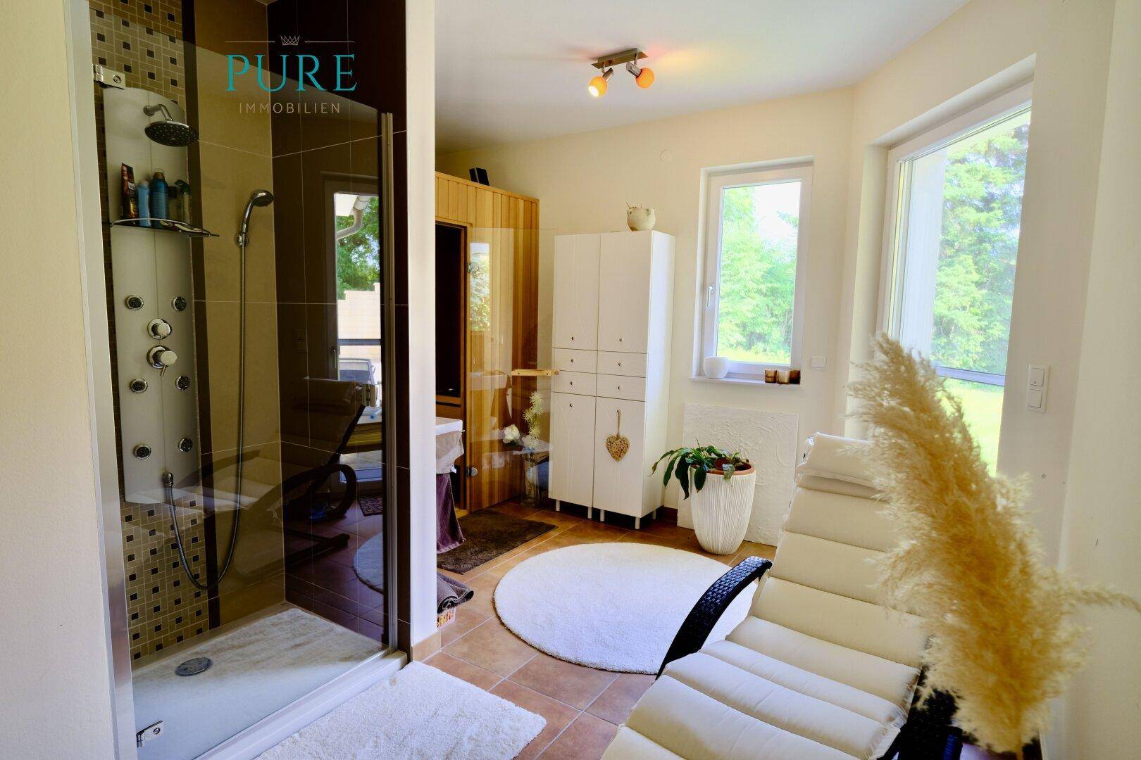 Modernes Badezimmer mit großer Dusche, Entspannungsliege und Zugang zur Sauna.