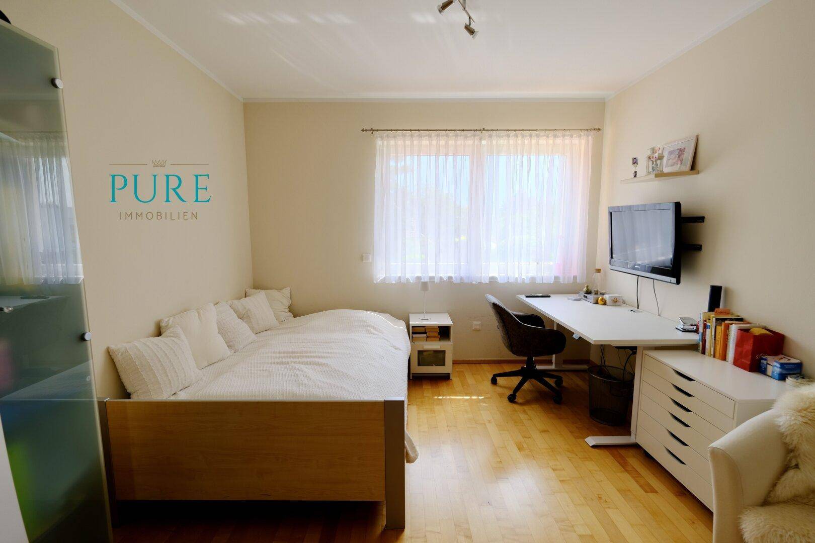 Gemütliches Schlafzimmer mit Holzboden, Bett, Schreibtisch und großem Fenster.