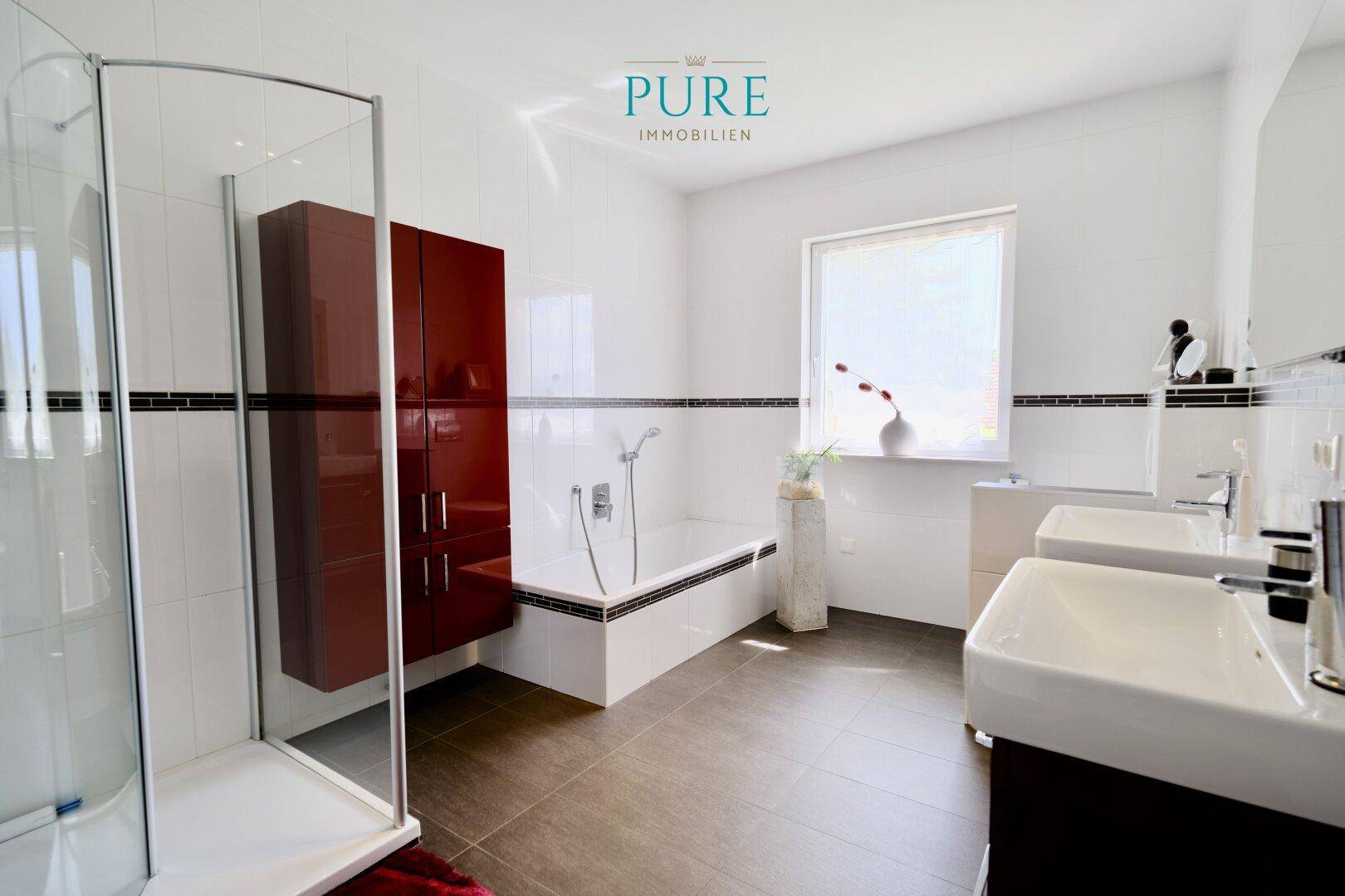Helles Badezimmer mit Doppelwaschbecken, Badewanne, Duschkabine und Fenster.
